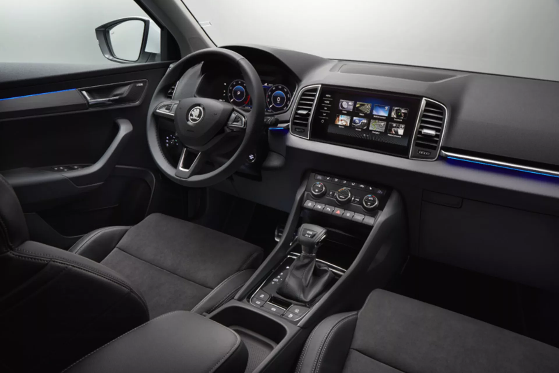 Interiér Škoda Karoq 2017 s výhľadom na palubnú dosku, dvere vodiča s ovládaním okien a zrkadiel, volant s tlačidlami pre multimédiá a tempomat, digitálno-analógový prístrojový panel, dotykový informačno-zábavný systém, klimatizáciu s duálnou reguláciou teploty, volič automatickej prevodovky, výber jazdných režimov a sedadlá potiahnuté kožou