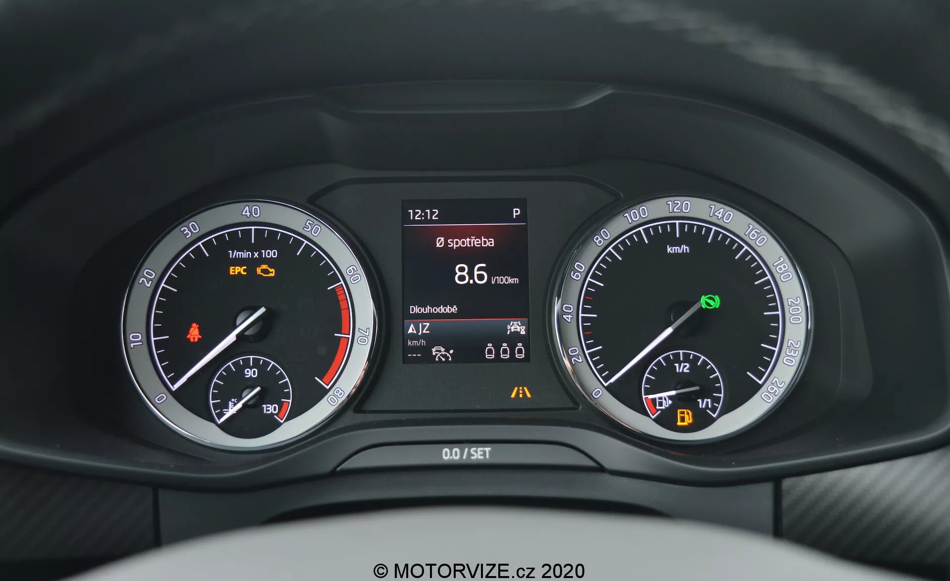 Priblížený pohľad vodiča na prístrojový panel vozidla Škoda Kodiaq 2017, zobrazujúci kombináciu analógových a digitálnych ukazovateľov za volantom. Prístrojová doska obsahuje otáčkomer s oranžovým výstražným svetlom, centrálny displej zobrazujúci rôzne informácie o vozidle, ako je čas, stav parkovacej brzdy, športový režim, dojazd a teplota, a rýchlomer s ukazovateľom paliva a indikátorom automatického štart/stopu.