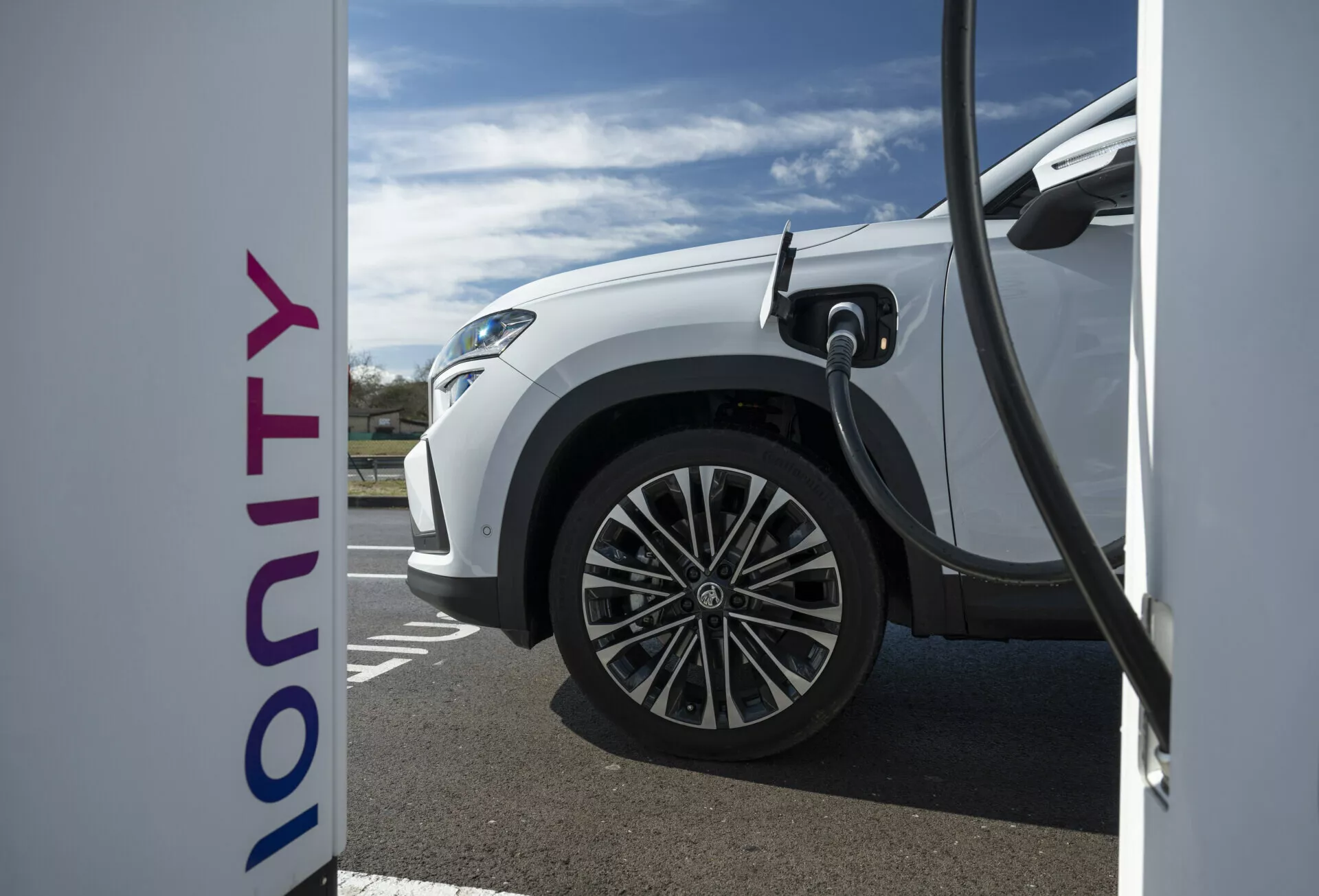 Detailný bočný pohľad na bielu elektrickú Škodu Kodiaq 2024 nabíjajúcu na stanici Ionity, zobrazujúci technológiu rýchleho nabíjania a moderný dizajn