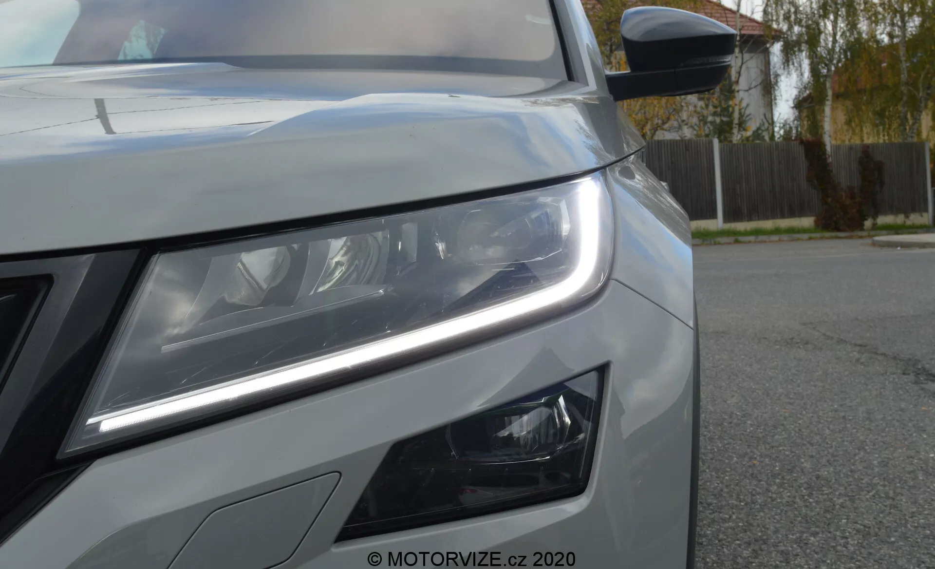 Detailný pohľad na prednú ľavú stranu vozidla Škoda Kodiaq 2017. Nízky uhol zdôrazňuje výrazné LED denné svetlá a detailné hlavné svetlomety naznačujúce pokročilú osvetľovaciu technológiu. Pod hlavným svetlometom sú viditeľné moderne navrhnuté hmlové svetlá. Na obrázku je tiež vidieť časť prednej mriežky, kovový náter s ostrými líniami karosérie a bočné zrkadlo s integrovaným smerovkovým indikátorom. Je prítomný vodoznak 'MOTORVIZE.cz 2020', ktorý označuje zdroj fotografie.