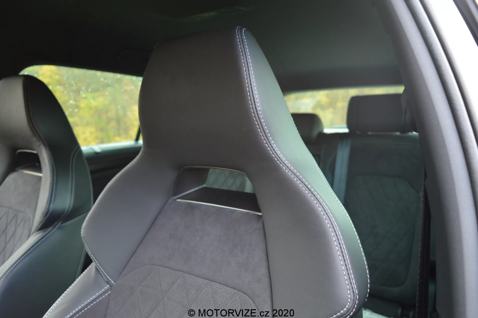 Interiér vozidla Škoda Kodiaq 2017 zameraný na predné vodičovo sedadlo z bočného pohľadu zozadu, zdôrazňujúci čalúnenie z kože a textúrovanej tkaniny s presným prešívaním po okrajoch. Moderne a športovo navrhnuté sedadlo má výrazné bočné opierky pre lepšiu podporu, integrovanú opierku hlavy a vzor šitia v tvare diamantu, ktorý naznačuje prémiovú estetiku. Pozadie interiéru je mierne rozmazané, aby sa zvýraznilo sedadlo.