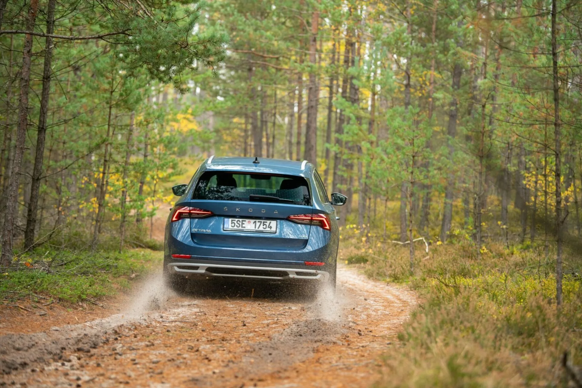 Modrá limuzína Škoda Octavia 2017 s LED zadnými svetlami, stieračom zadného okna a dvojitým výfukom na lesnej ceste s dynamickým vznášaním prachu naznačujúcim schopnosti pohonu všetkých kolies