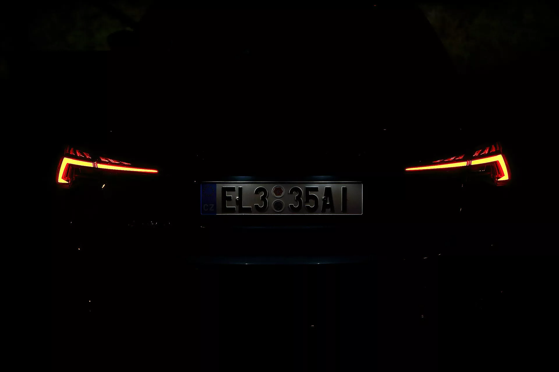 Zadný pohľad na Škoda Octavia 2020 Limousine, fotografovaný v noci alebo v slabo osvetlenom prostredí. Obrázok sa sústreďuje na osvetlené zadné svetlá a ŠPZ, ktoré ukazujú moderný a uhlový dizajn. Detaily vozidla sú kvôli nízkemu osvetleniu skryté, čím sa zdôrazňuje elegantná a súčasná zadná časť.