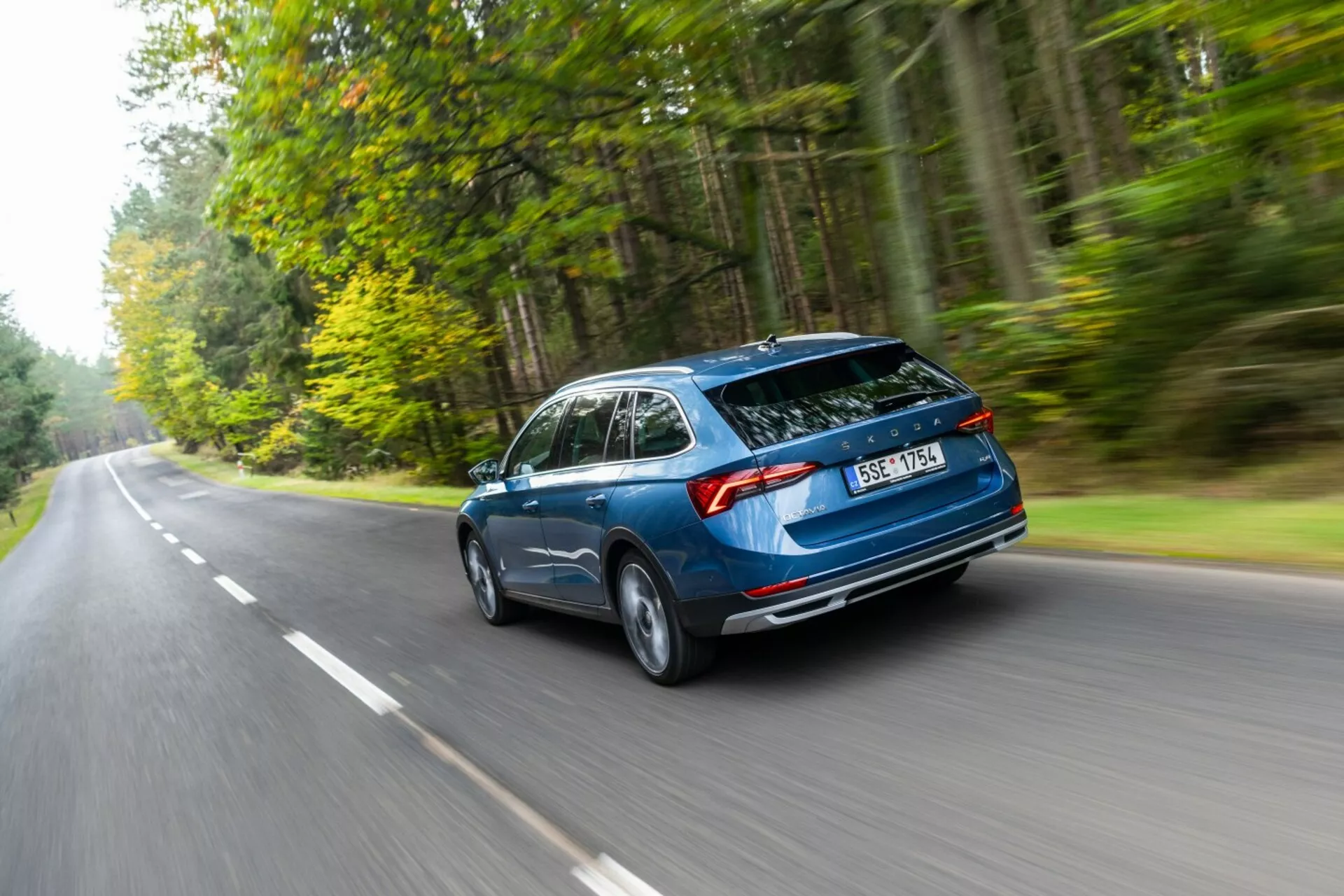Pohybujúce sa kombi Skoda Octavia 2017 zachytené z zadného trojštvrťového uhla zdôrazňujúce aerodynamický dizajn, zadný kufor hatchback a horizontálne zadné svetlá na ceste lemovanej lesom