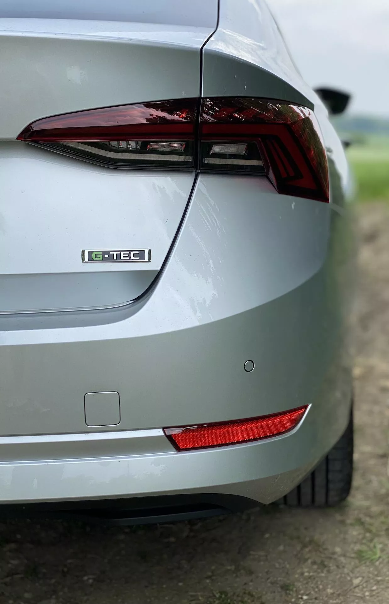 Detailný šikmý pohľad na pravú zadnú časť strieborného vozidla Škoda Octavia Limousine 2020. Obrázok zvýrazňuje zadné svetlo, označenie G-TEC, elegantný dizajn kufra, zadný nárazník, zadný odrazka a metalický lak. Rozmazané pozadie zameriava pozornosť na dizajnové prvky vozidla.