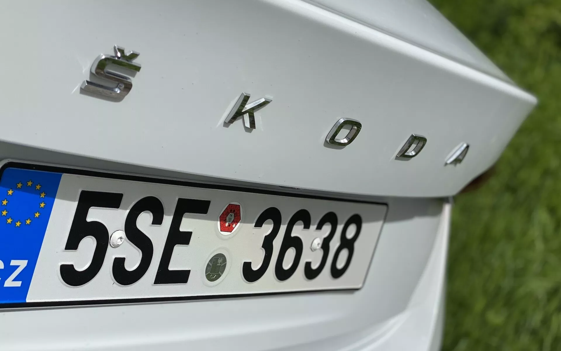 Detailný čiastočný zadný pohľad na Škoda Octavia 2020 limuzína so zameraním na veko batožinového priestoru, zadnú ŠPZ s európskym identifikátorom 'CZ' a chrómovaným nápisom 'SKODA'. Funkcie zahŕňajú štyri kruhové parkovacie senzory nad ŠPZ na asistenciu pri manévrovaní vozidla.