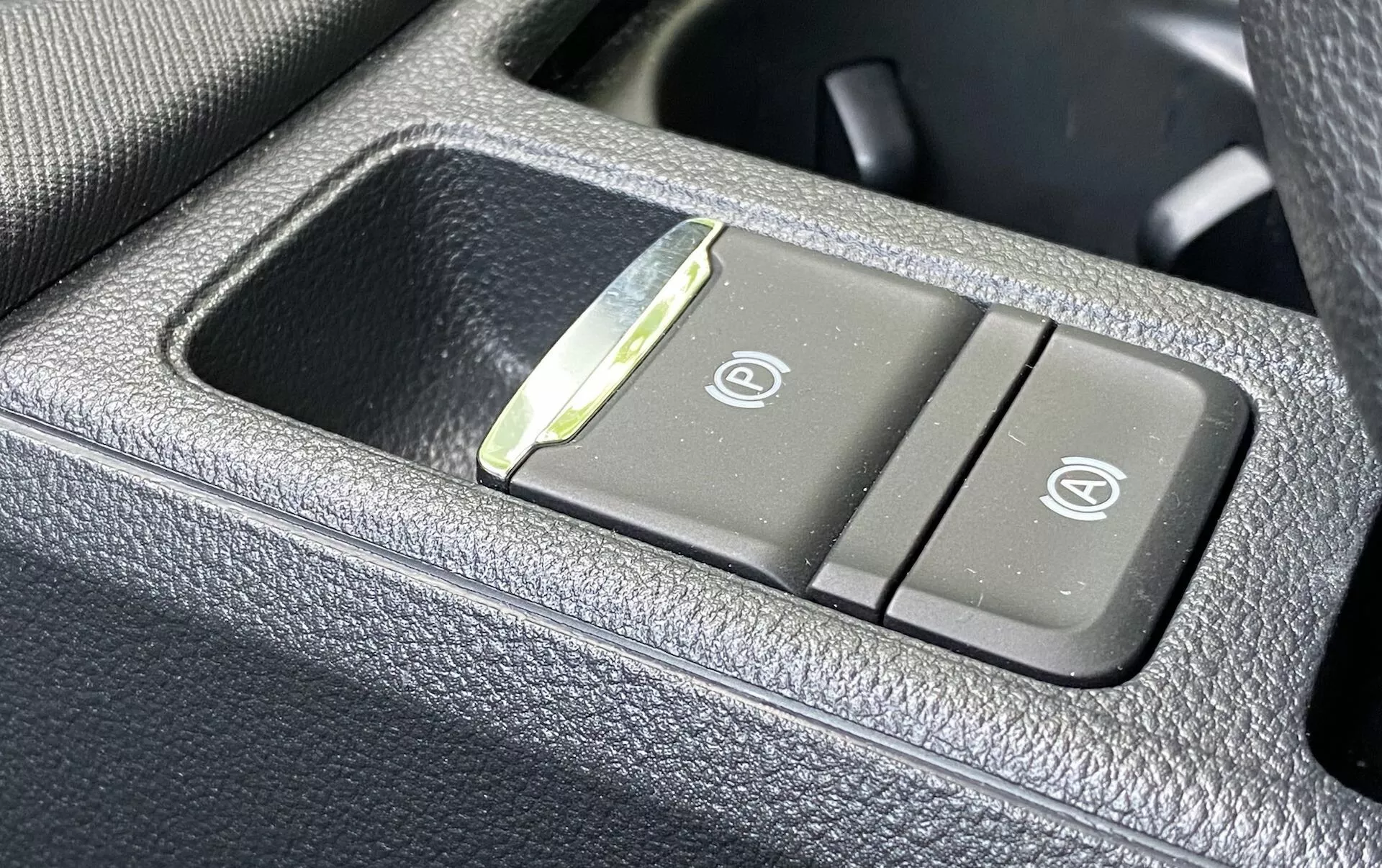 Detailný pohľad na ovládací panel v interiéri vozidla Škoda Octavia 2020, zobrazujúci tlačidlá vyhrievaných a ventilovaných sedadiel na tmavom, zrnitom, koženkovom materiáli. Ľavé tlačidlo má ikonu vyhrievaného sedadla a pravé tlačidlo zobrazuje ikonu ventilovaného sedadla, medzi tlačidlami je malý LED indikátor.