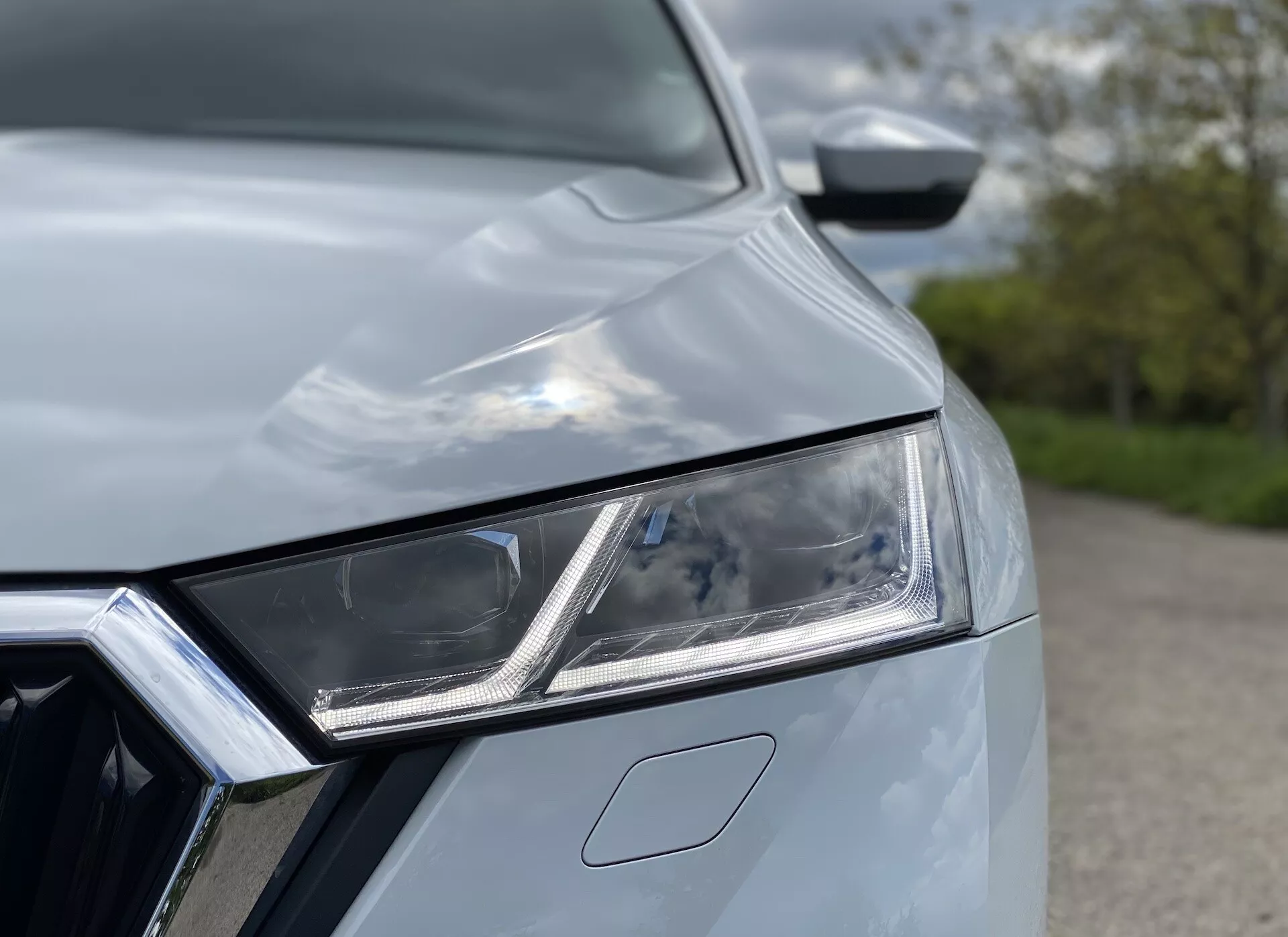 Detailný pohľad na vozidlo Škoda Octavia Limousine 2020, zameraný na zložitý ľavý predný svetlomet s LED prvkami a denným svietením. Viditeľná je časť chrómovaného grilu a kapota s aerodynamickými krivkami, čo vytvára moderný a štýlový vzhľad s prvotriednou technológiou a dizajnom.