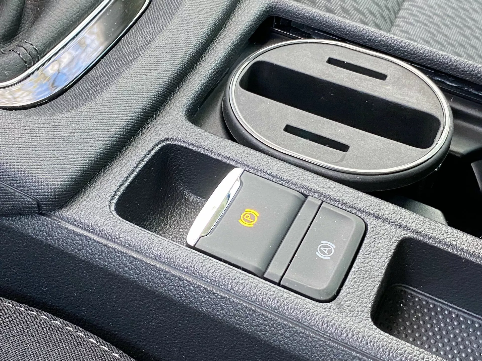 Detailný pohľad na stredovú konzolu Škoda Octavia 2020 s bezdrôtovou nabíjacou podložkou, tlačidlom na recirkuláciu vzduchu, tlačidlom zabezpečenia vozidla, čiastočne otvorenou priehradkou s gumovou podšívkou a radiacou pákou s chrómovým akcentom.