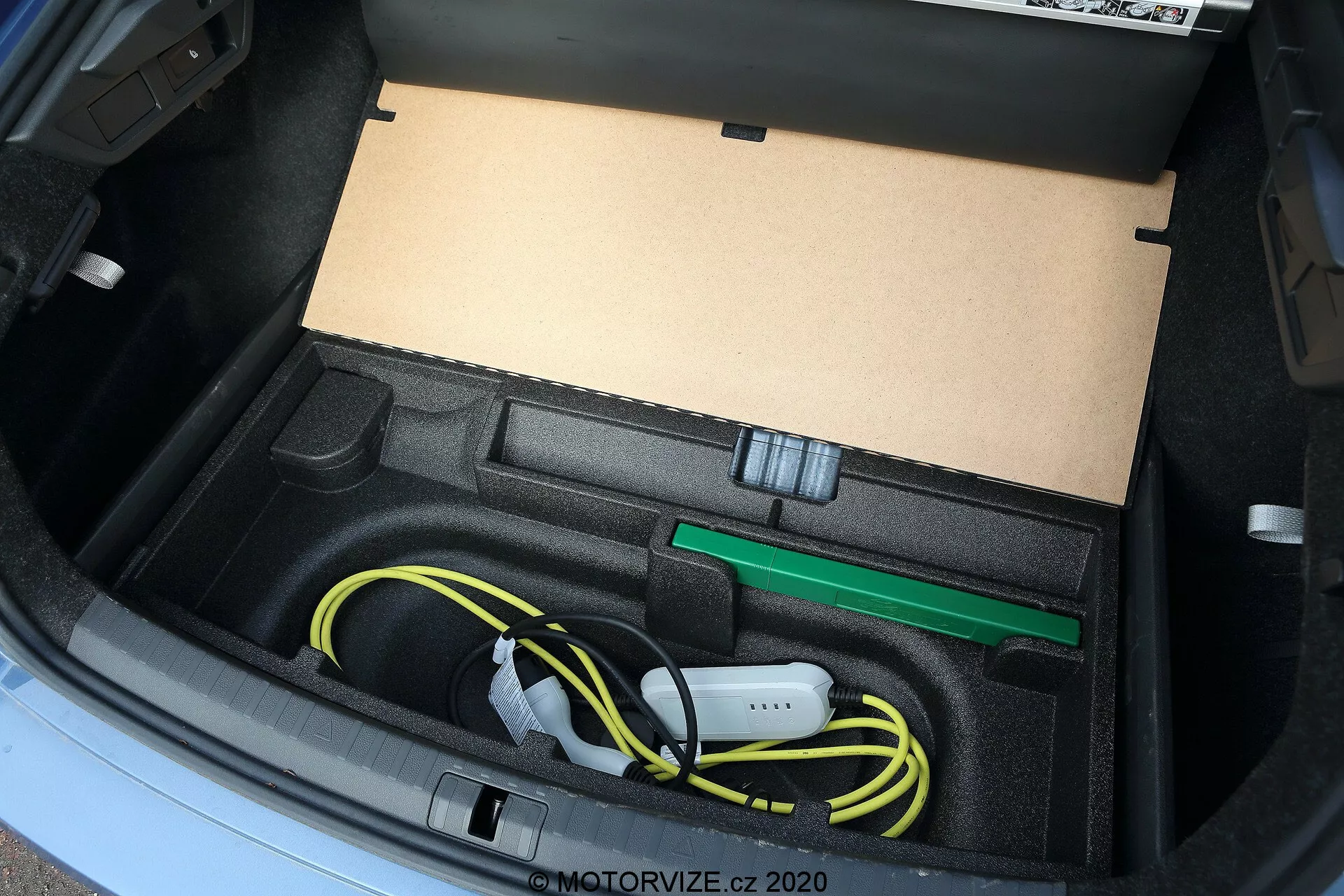 Detailný pohľad na kufor vozidla Škoda Octavia 2020, zobrazujúci na mieru prispôsobenú priehradku na uloženie nabíjacieho kábla a príslušenstva elektromobilu, vrátane starostlivo zvinutého žltého nabíjacieho kábla a zeleného ťažného oka, zachytený z vysokého uhla s prirodzeným osvetlením.