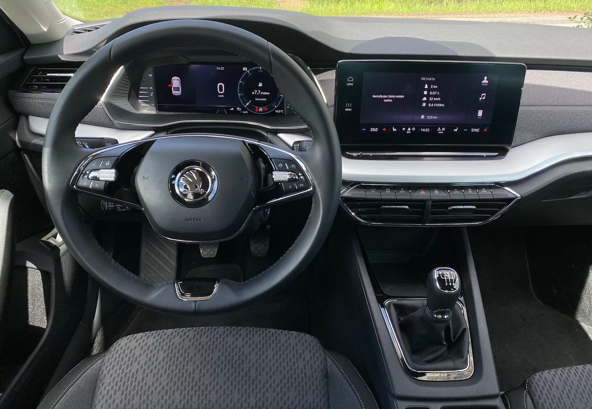 Pohľad na interiér sedanu Škoda Octavia 2020 z perspektívy sedadla spolujazdca, zvýrazňujúci multifunkčný trojramenný volant s rôznymi ovládačmi pre médiá a hands-free hovory, digitálny prístrojový panel pre navigáciu a údaje o vozidle, centrálny dotykový infotainment, kompaktnú automatickú prevodovku, kovové akcenty na ventiláciách a infotainmentovom systéme, odolné textilné čalúnenie na sedadle vodiča a prispôsobiteľné ambientné osvetlenie.