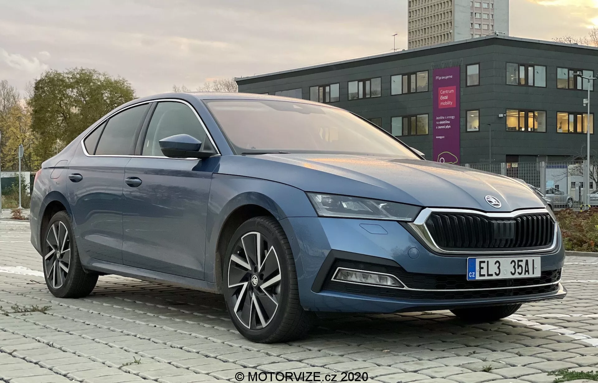 Profesionálna fotografia štvordverového vozidla Skoda Octavia Limousine 2020 vyfotografovaná z trojštvrťového uhla spredu zľava, jasne ukazuje charakteristickú mriežku, elegantné LED svetlomety, predný nárazník s možnými hmlovými svetlami, hladké línie karosérie, viaclúčové hliníkové kolesá, integrované smerovky v bočných zrkadlách a prémiové chrómové orámovanie okien v mestskom alebo prímestskom prostredí za úsvitu alebo súmraku.