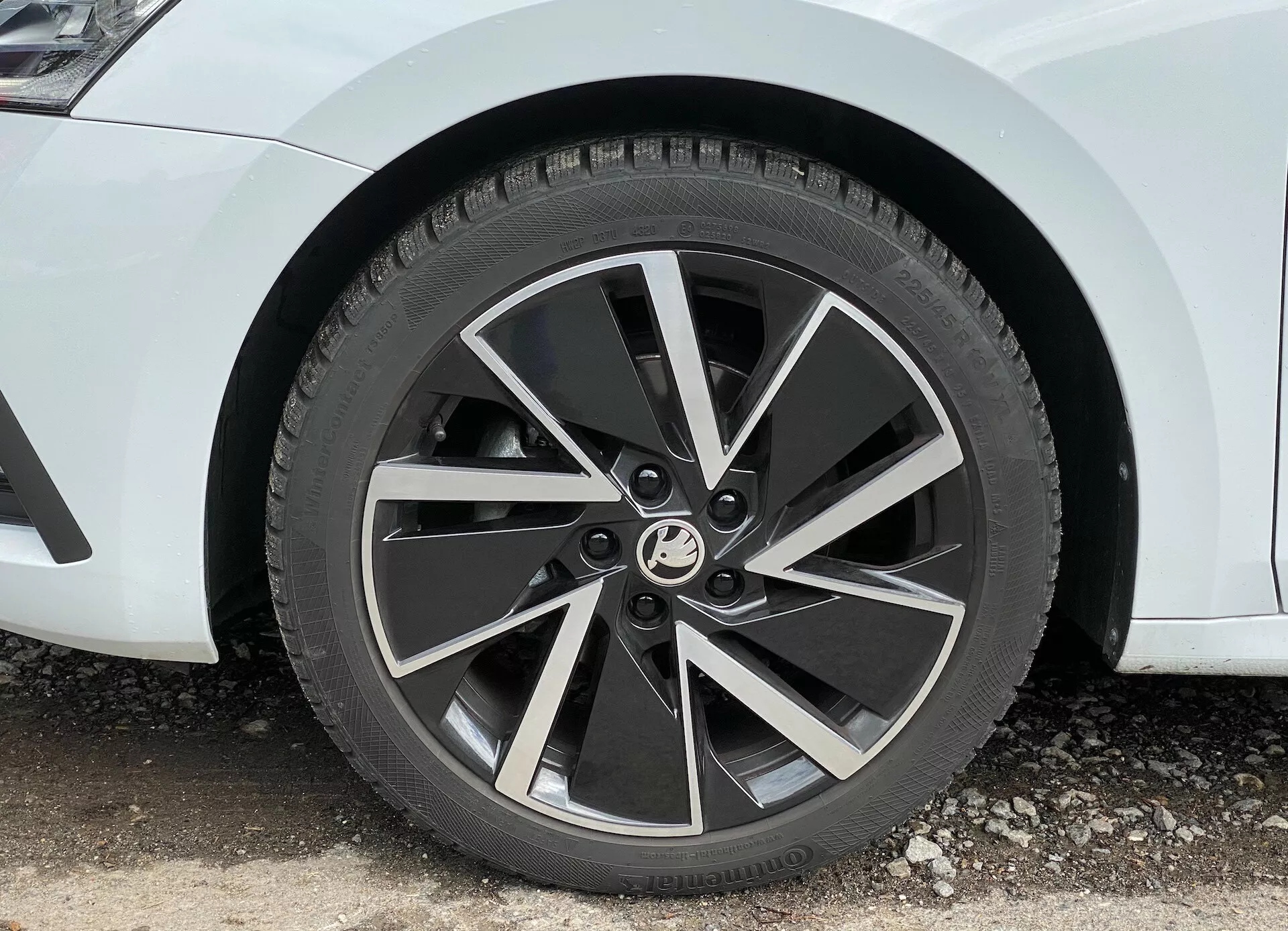 Detailný záber na predné koleso auta Škoda Octavia limuzína 2020, ukazujúci moderný päťramenný hliníkový disk s dvojfarebným povrchom a opracovanými miestami na rámoch, zachytený v uhle 45 stupňov, zvýrazňujúci jeho dynamický, turbínový dizajn a viditeľný dezén celosezónnej pneumatiky.