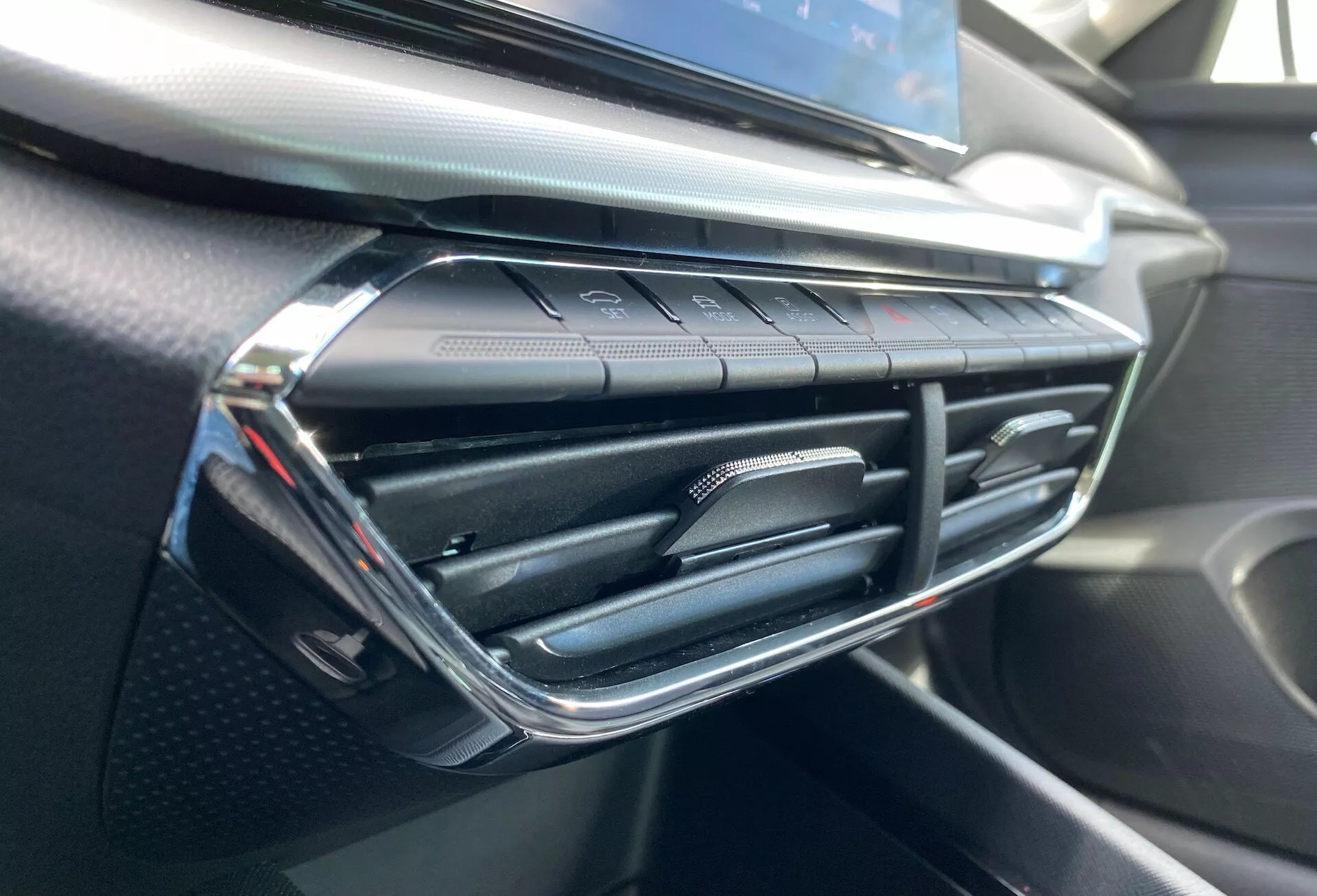 Detailný pohľad na interiér vozidla Škoda Octavia 2020 so zameraním na ventiláciu klimatizácie a okolitú oblasť prístrojovej dosky, s moderným dizajnom vetracích otvorov s chrómovými akcentami a dotykovými tlačidlami na ovládanie klimatizácie pod nimi, s mäkkým a štruktúrovaným prístrojovým panelom pripomínajúcim uhlíkové vlákno.