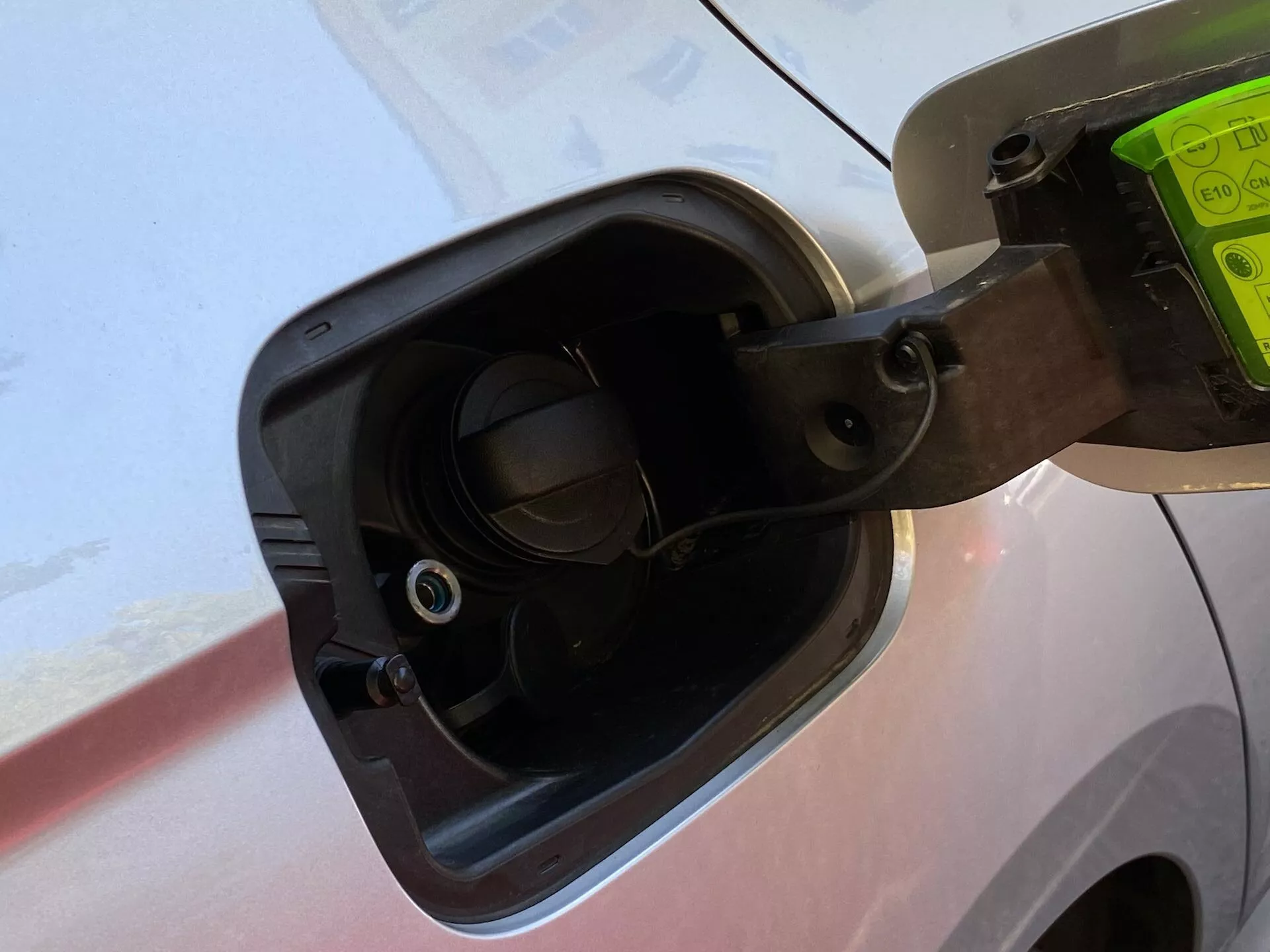 Detailný záber na plniaci otvor paliva u modelu Skoda Octavia Limousine 2020, zobrazujúci otvorený uzáver paliva pripevnený pružným popruhom, okolité detaily karosérie vozidla a zapustený plniaci hrdlo s viditeľným ventilom, všetko snímané z mierneho uhla zhora.