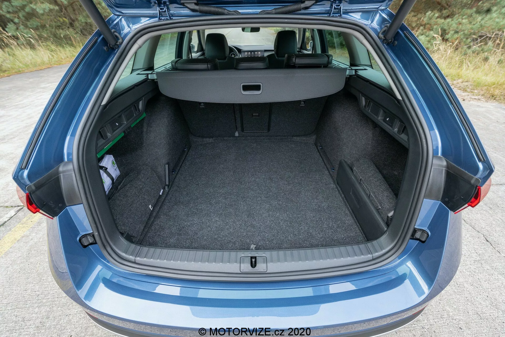 Detailný pohľad na otvorený kufor moderného modelu Škoda Octavia Scout 2020 s plne otvoreným výklopným dizajnom. Obrázok zachytáva kufor od zadného nárazníka po zadné čelné sklo, vrátane časti strechy. Kobercový nákladný priestor má rovnú nakladaciu plochu a malý úložný priestor vľavo. Zadné sedadlá sú v normálnej polohe s rozvinutou zatahovateľnou krytkou kufra, ktorá skrýva predmety v kufri.