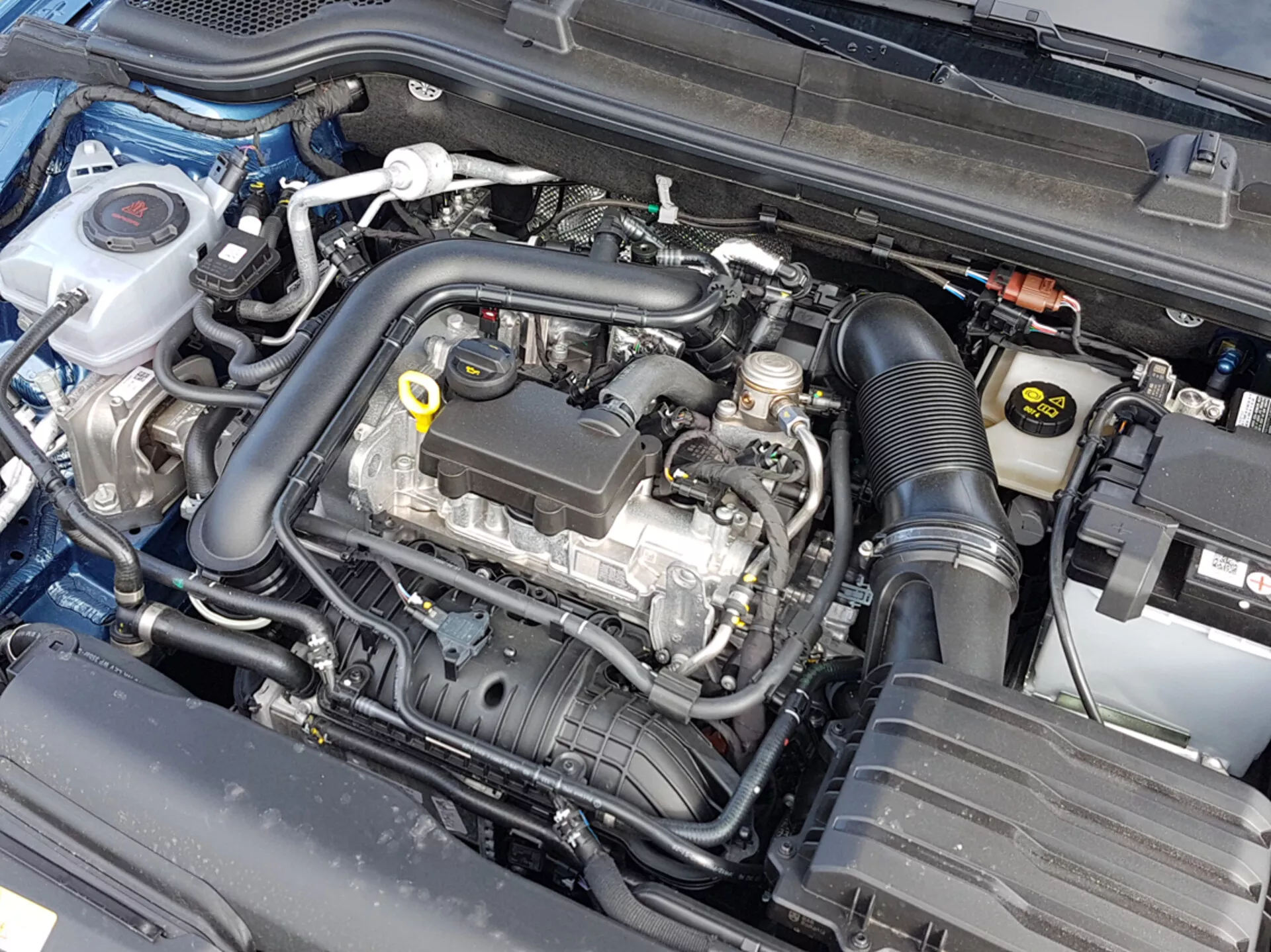 Detailný pohľad na motorový priestor Škoda Scala 2019 s otvorenou kapotou, zobrazujúci motorový blok a rôzne komponenty ako je nádoba na chladiacu kvapalinu, púzdro vzduchového filtra a batéria, čo naznačuje zameranie na automobilové inžinierstvo a údržbu.