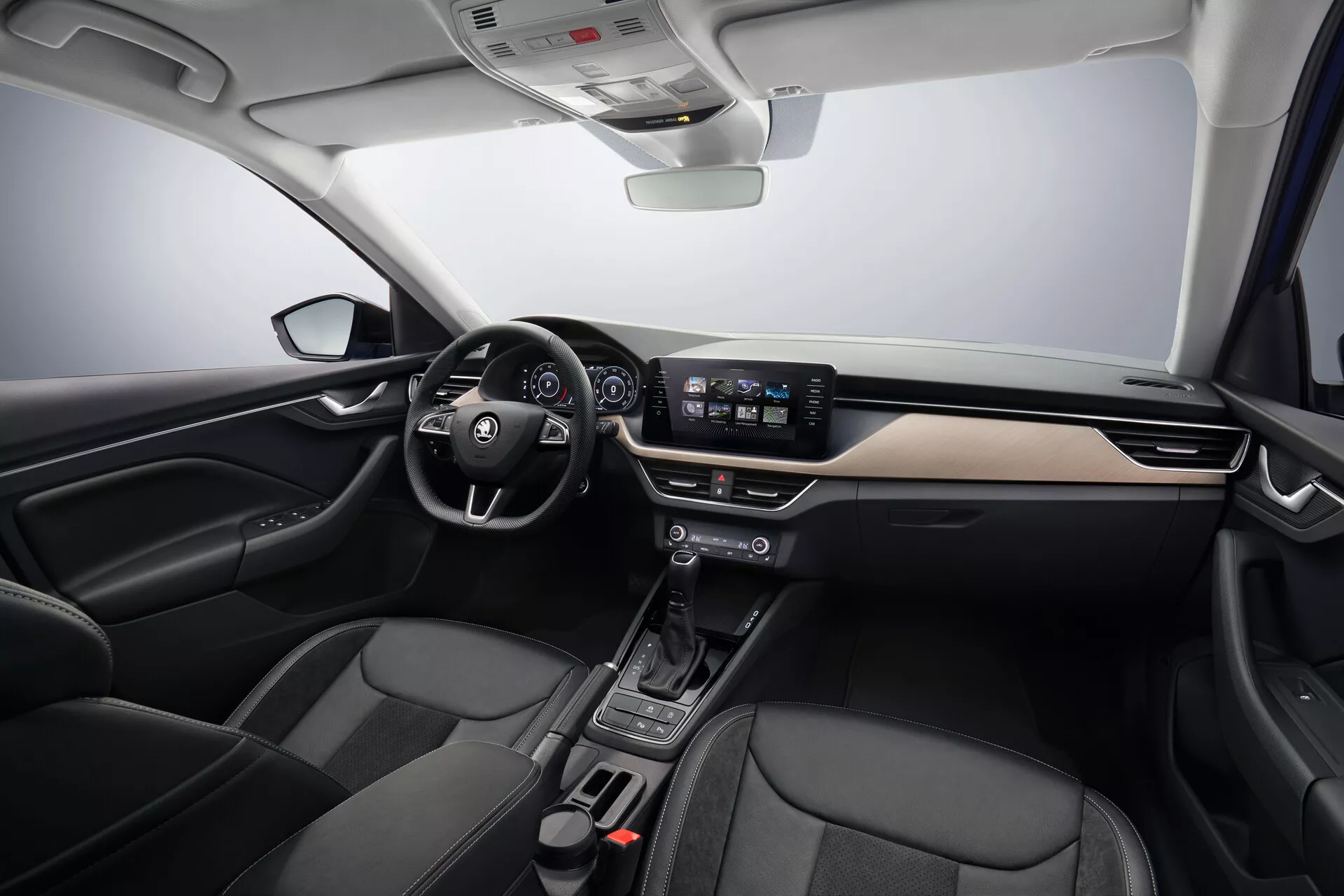 Interiér Škoda Scala 2019 ukazujúci moderný dizajn kokpitu s akcentmi z kefovaného kovu, centrálnym dotykovým informačným systémom, minimalistickými ovládačmi klímy a prednými sedadlami potiahnutými kožou, pohľad z centrálného predného uhla.