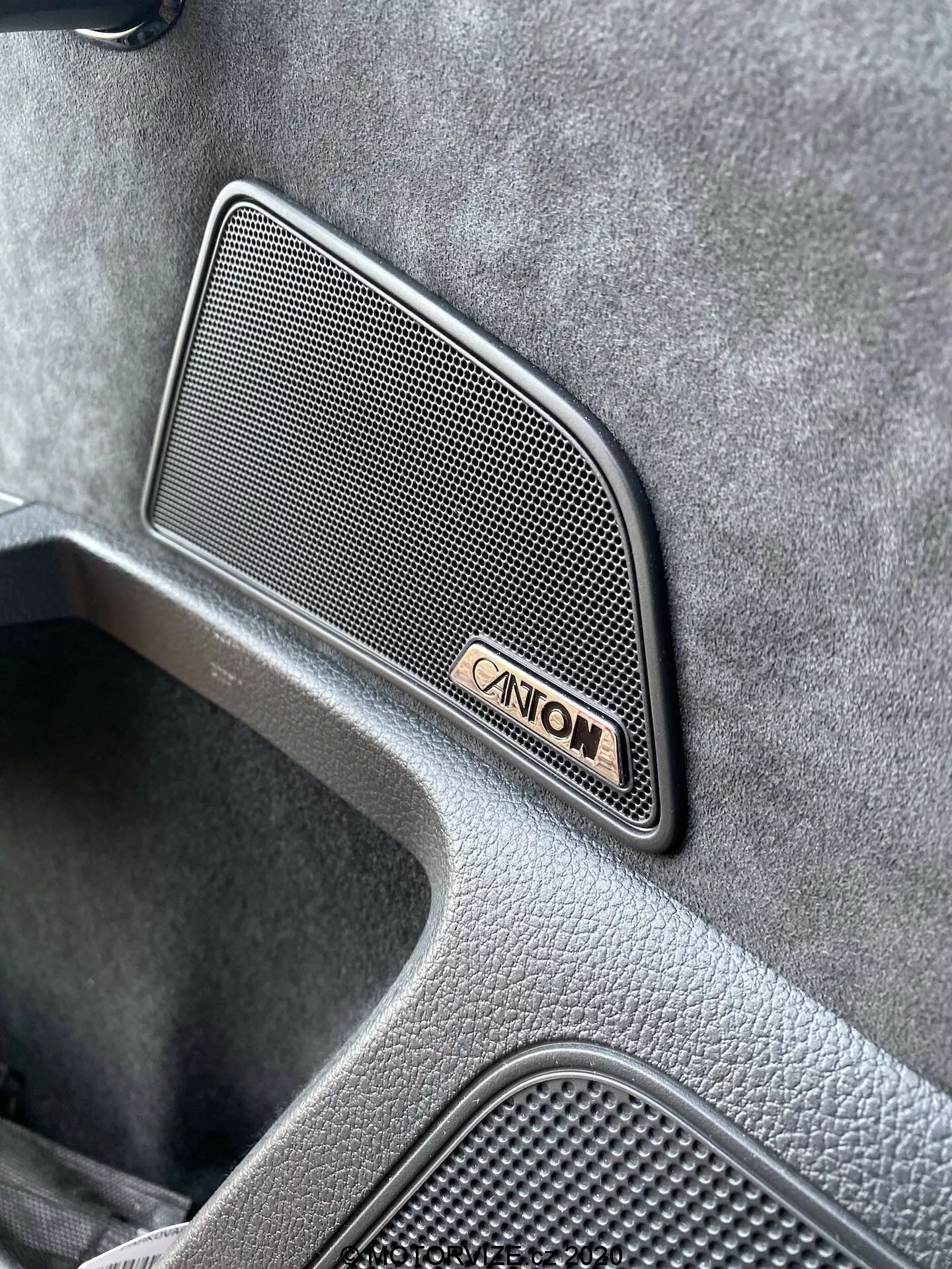 Detailný pohľad na interiér modelu Škoda Superb Limousine 2019, zdôrazňujúci prémiovú mriežku reproduktora značky Canton so sieťovým vzorom lichobežníkového tvaru umiestnenú na dverovom paneli, doplnenú o znak Canton a ukazujúcu vysokokvalitnú textúrovanú povrchovú úpravu a zapustenú oblasť naznačujúcu dizajn luxusného vozidla.