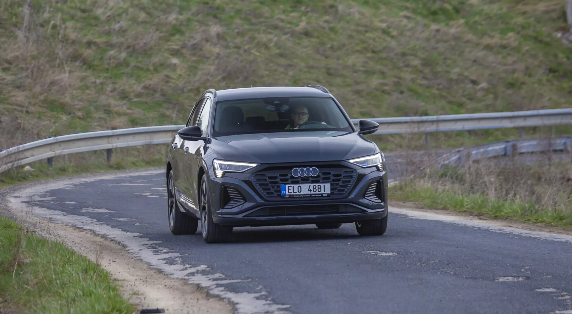 Škoda Superb Limuzína 2015 v pohybe na zakrivenom ceste, zobrazuje jej šesťuholníkovú mriežku s logom kruhov Audi, LED denné svetlá a aerodynamický tvar s vytesanými líniami kapoty, bočný pohľad zahŕňajúci zliatinové kolesá.