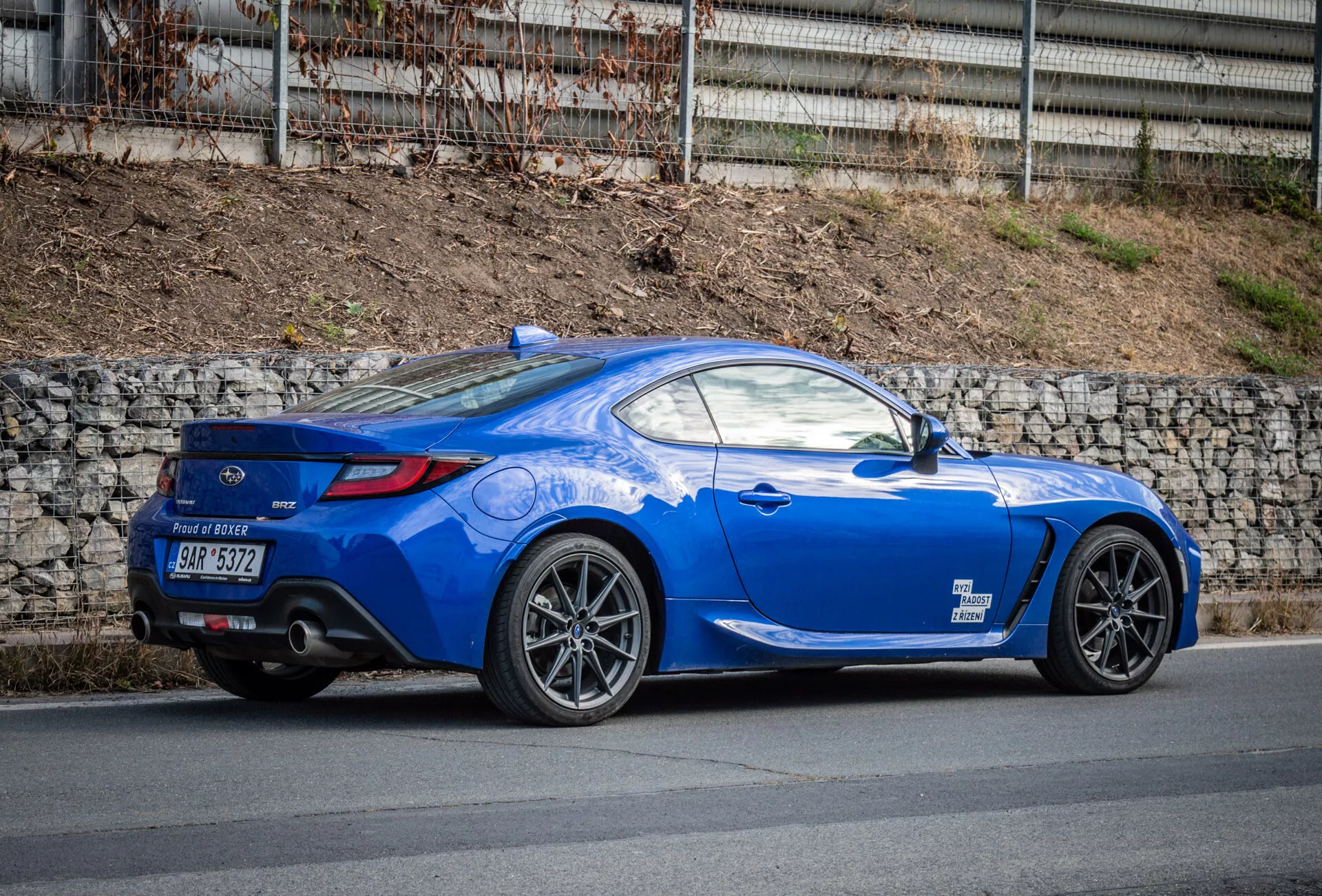 Športové kupé Subaru BRZ 2023 vo svetlomodrej farbe s aerodynamickým dizajnom zaparkované na ulici, zdôrazňujúce zadný blatník, zadné svetlá, zakrivenie zadného okna smerom k veku kufra, tvarované línie, sklonenú strechu, viaceročné zliatinové kolesá, výkonné brzdy, nízky zadný spojler, dvojité výfukové potrubia v zadnom difúzore, zrkadlá v farbe karosérie a športovú dlhú kapotu.