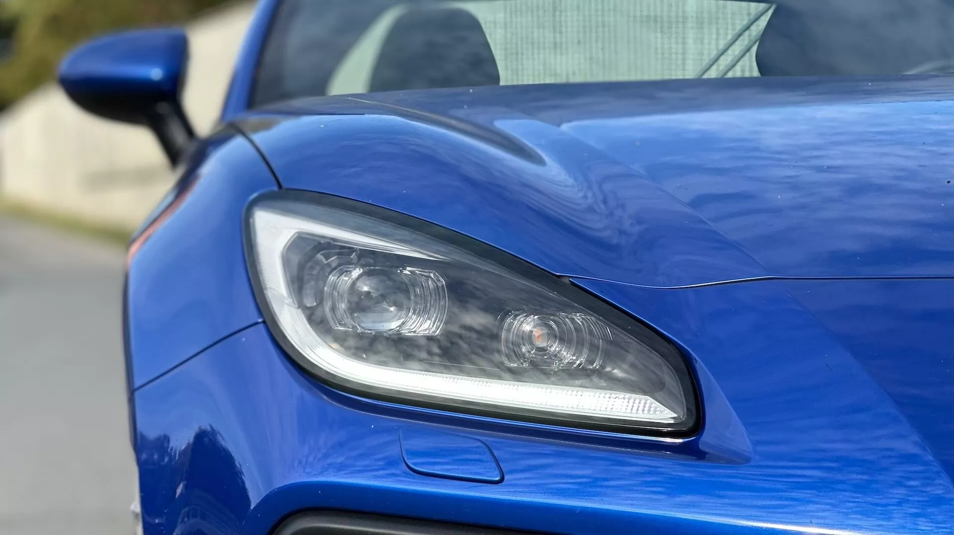 Detailný pohľad na predné svetlo vodiča Subaru BRZ 2023, predstavujúci dizajn osvetlenia LED alebo HID, projekčné šošovky a športový vzduchový vstup na metalickom modrom karosérii