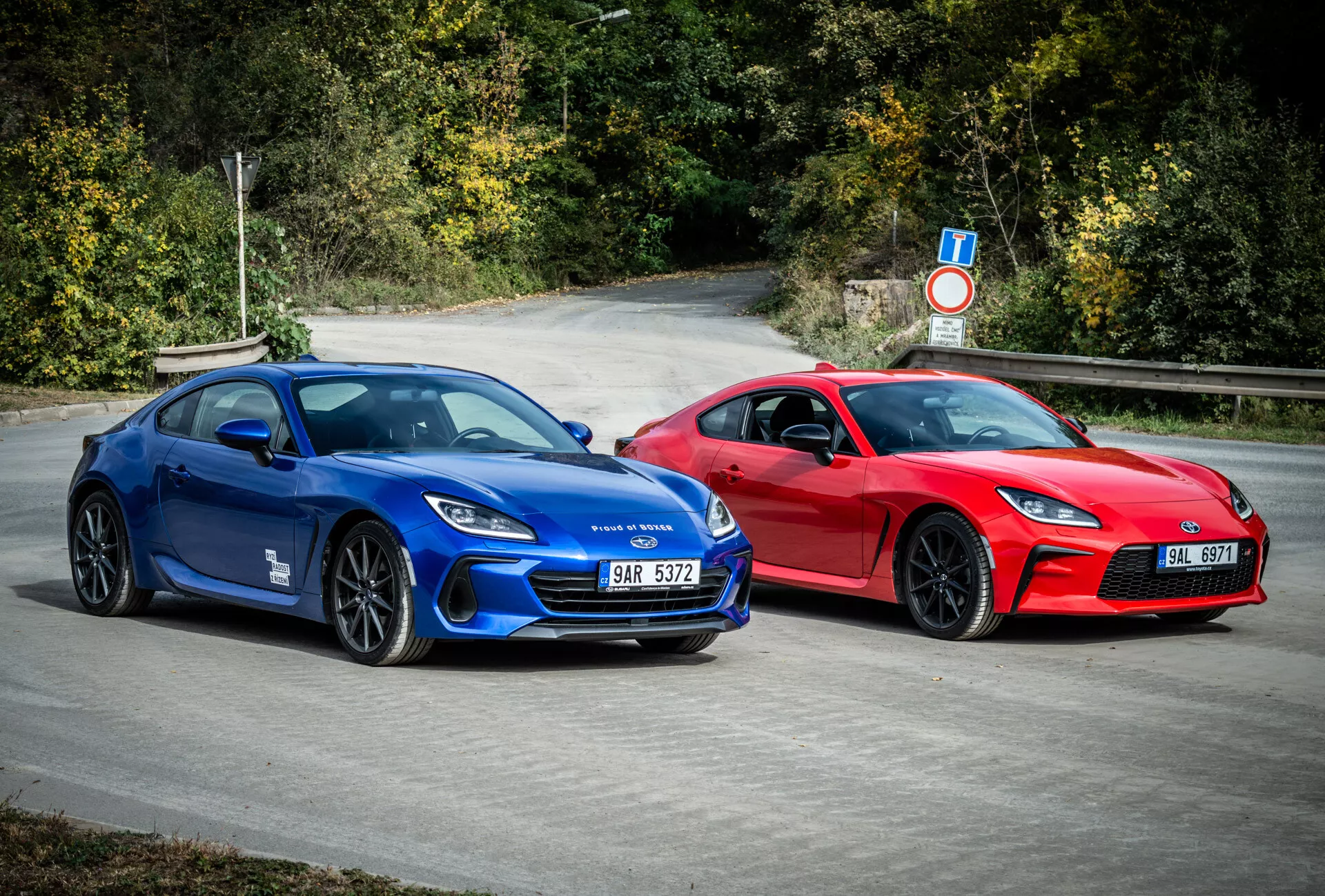 Športové kupé Subaru BRZ 2023 v modrej a červenej farbe s aerodynamickým dizajnom a výkonnostnými prvkami, zaparkované vonku v prírodnom prostredí