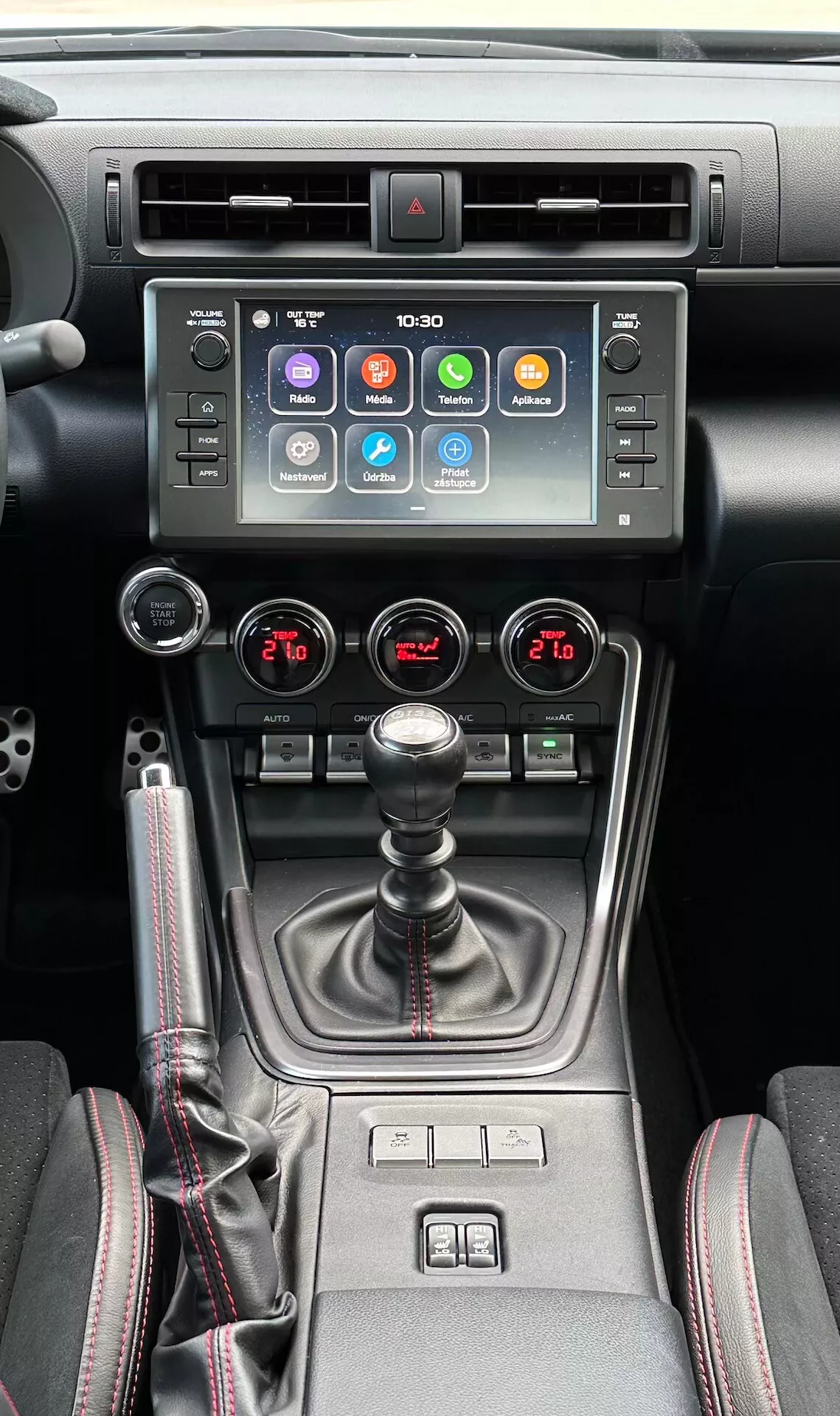 Interiér Subaru BRZ 2023 zameraný na stredovú konzolu, ktorá obsahuje dotykovú obrazovku infotainmentu, indikátor výstražného svetla, kovové vzduchové venty, dvojzónovú klimatizáciu, manuálnu prevodovku so koženým čižmou, ovládače vyhrievania sedadiel a multimódny vodičský selektor v modernom čiernom a kovovom dizajne.