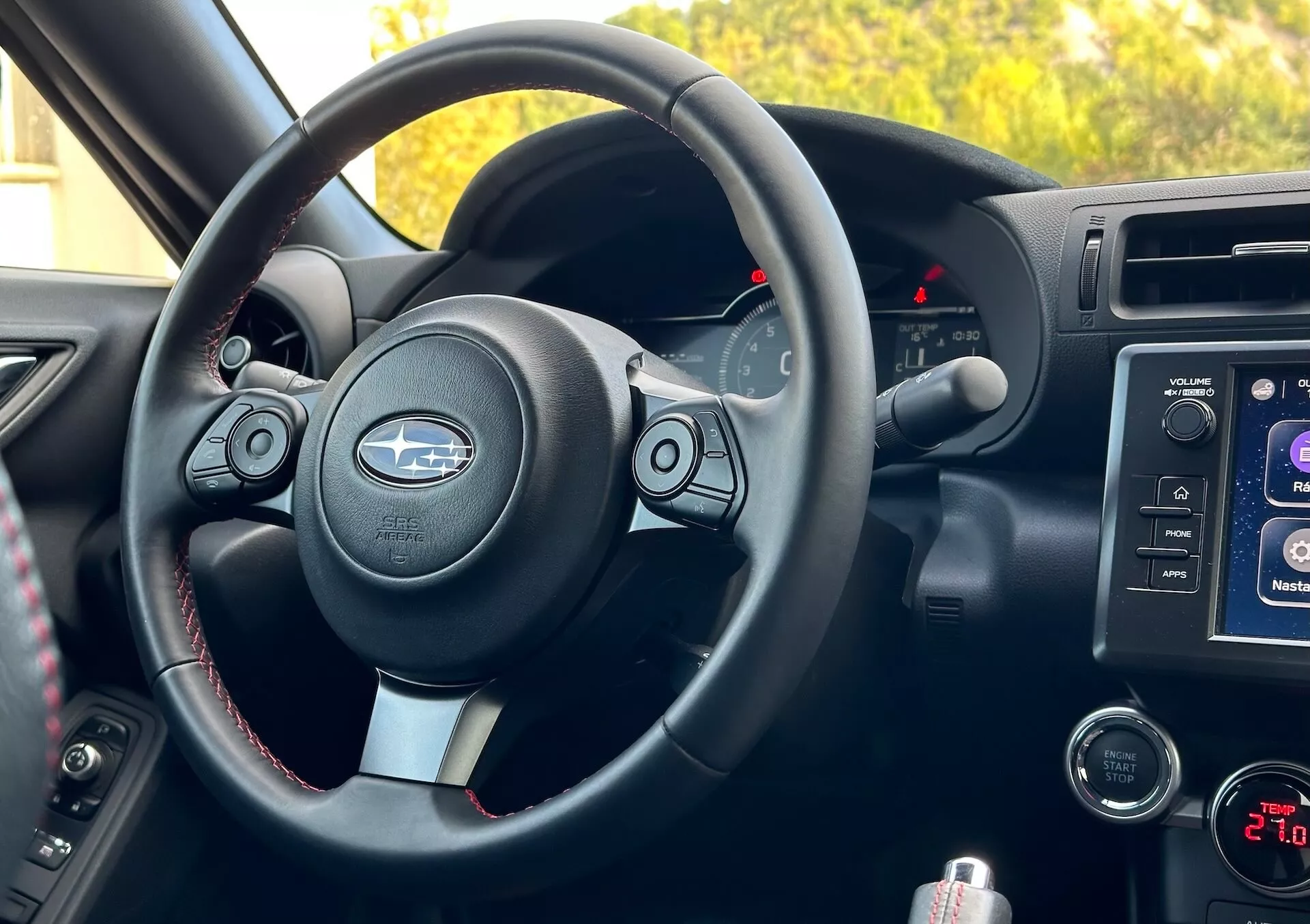 Interiér Subaru BRZ 2023 z pohľadu spolujazdca s volantom s kovovými akcentmi a logom Subaru, ovládacími tlačidlami, kontrastným stehovaním, prístrojovou doskou s podsvietenými ukazovateľmi, centrálnou konzolou s infotainment systémom, ovládaním audia a klímy a úložným priestorom.