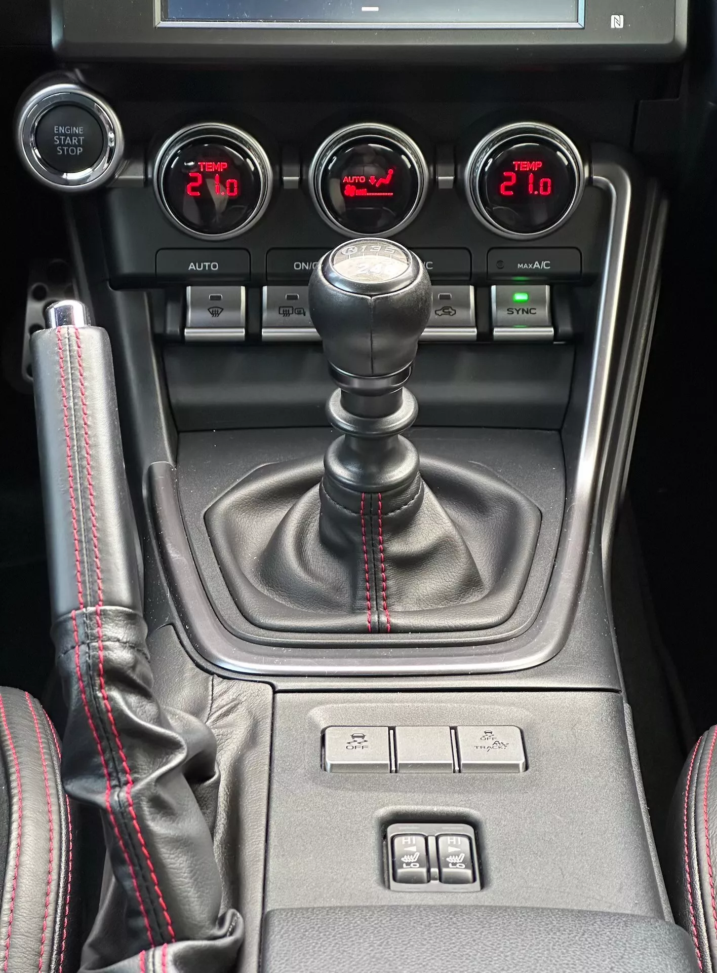 Centrálna konzola Subaru BRZ 2023 s manuálnou prevodovkou so športovým červeným stehom, pomocnými ukazovateľmi pre tlak turbodúchadla, napätie batérie, teplotu oleja a duálnu klimatizáciu v detailnom pohľade interiéru