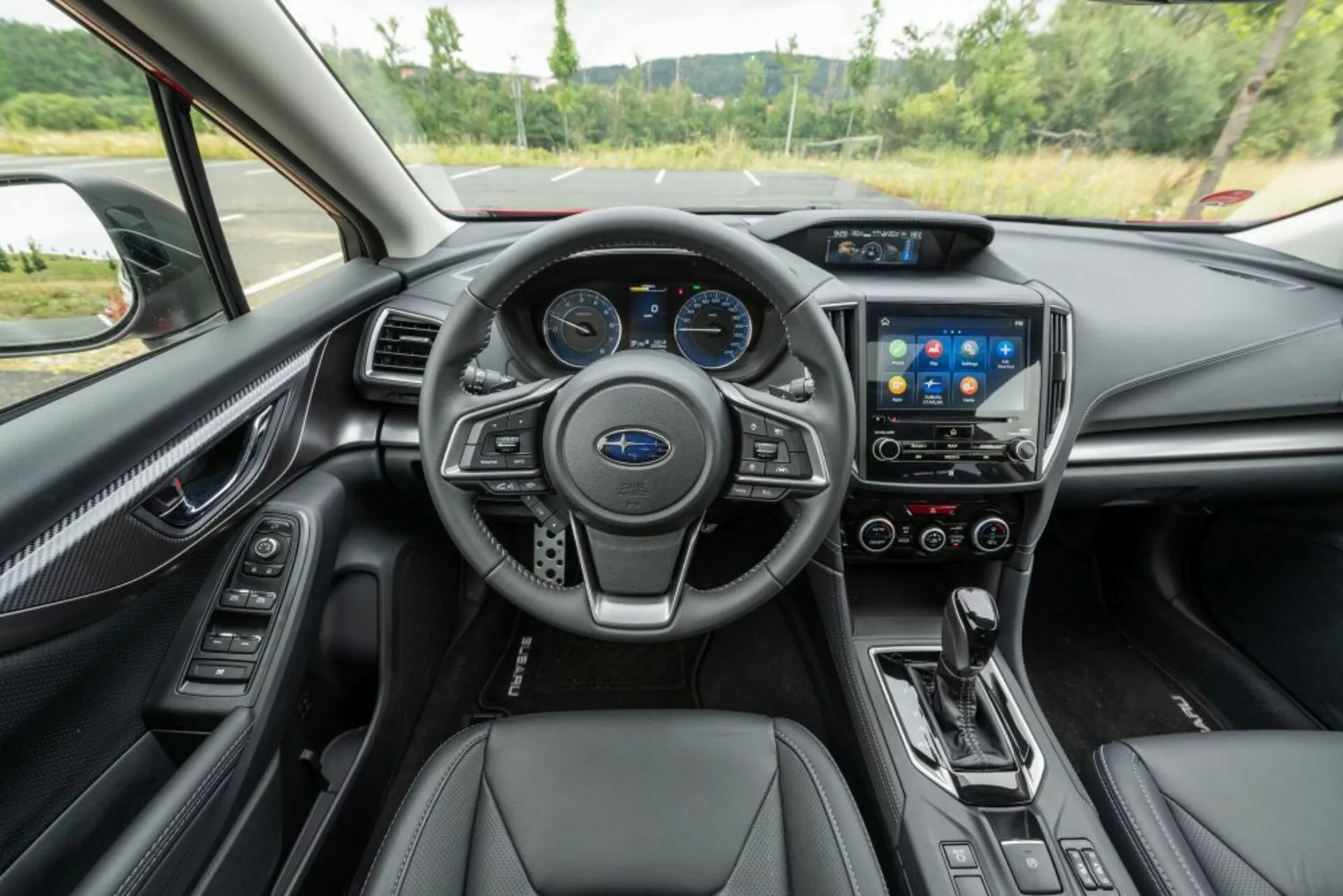 Interiér Subaru Impreza 2018 s výhľadom na volant s ovládacími prvkami, digitálnym prístrojovým panelom, dotykovým systémom infotainment, ovládaním klimatizácie, radiacou pákou automatickej prevodovky a koženými sedadlami s prémiovými dekoráciami z pohľadu vodiča