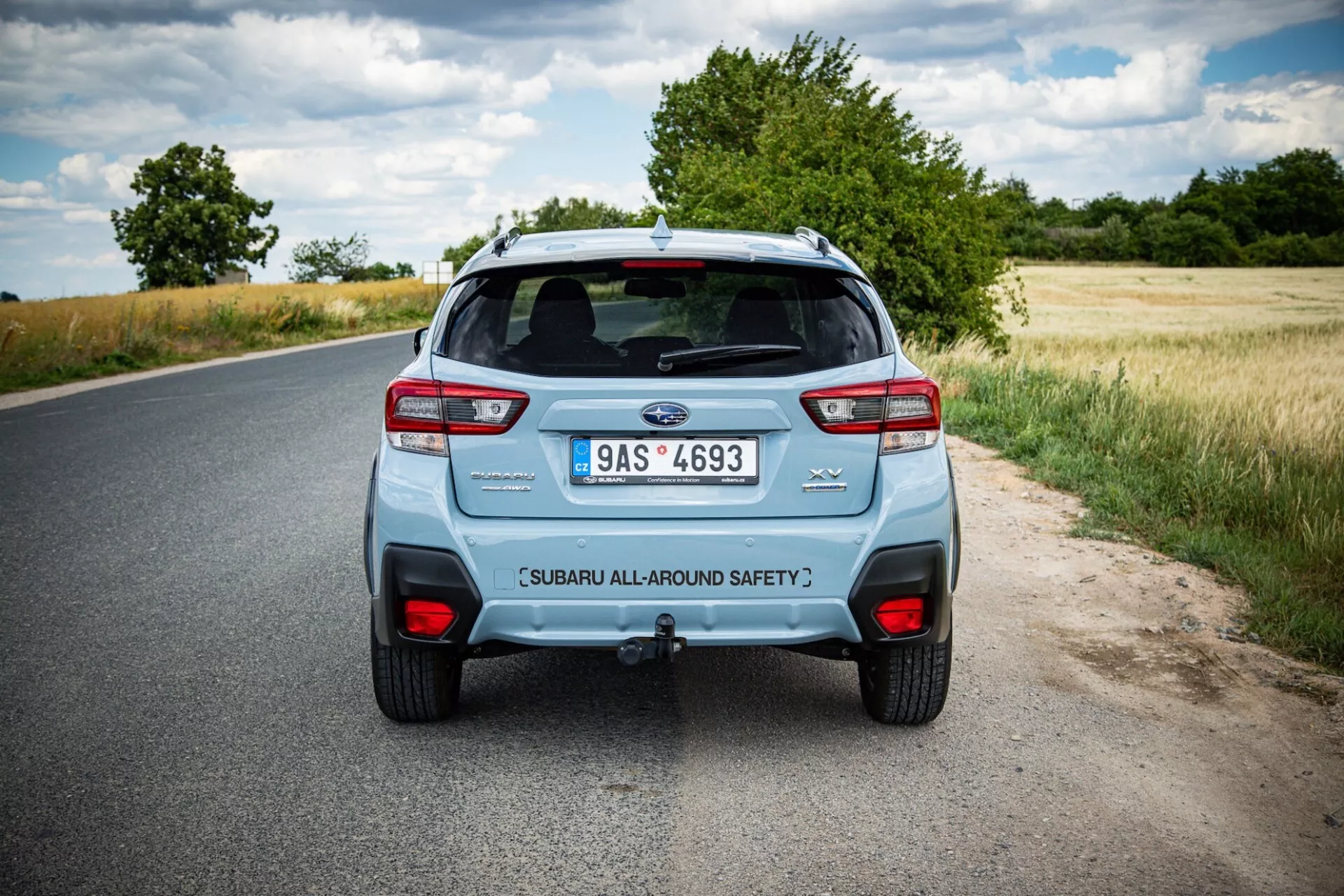 Zadný pohľad na Subaru XV 2021 na vidieckej ceste, ukazuje charakteristické zadné svetlá auta, dvojitý výfukový systém a veko batožinového priestoru s bezpečnostným označením pod čiastočne zamračenou oblohou