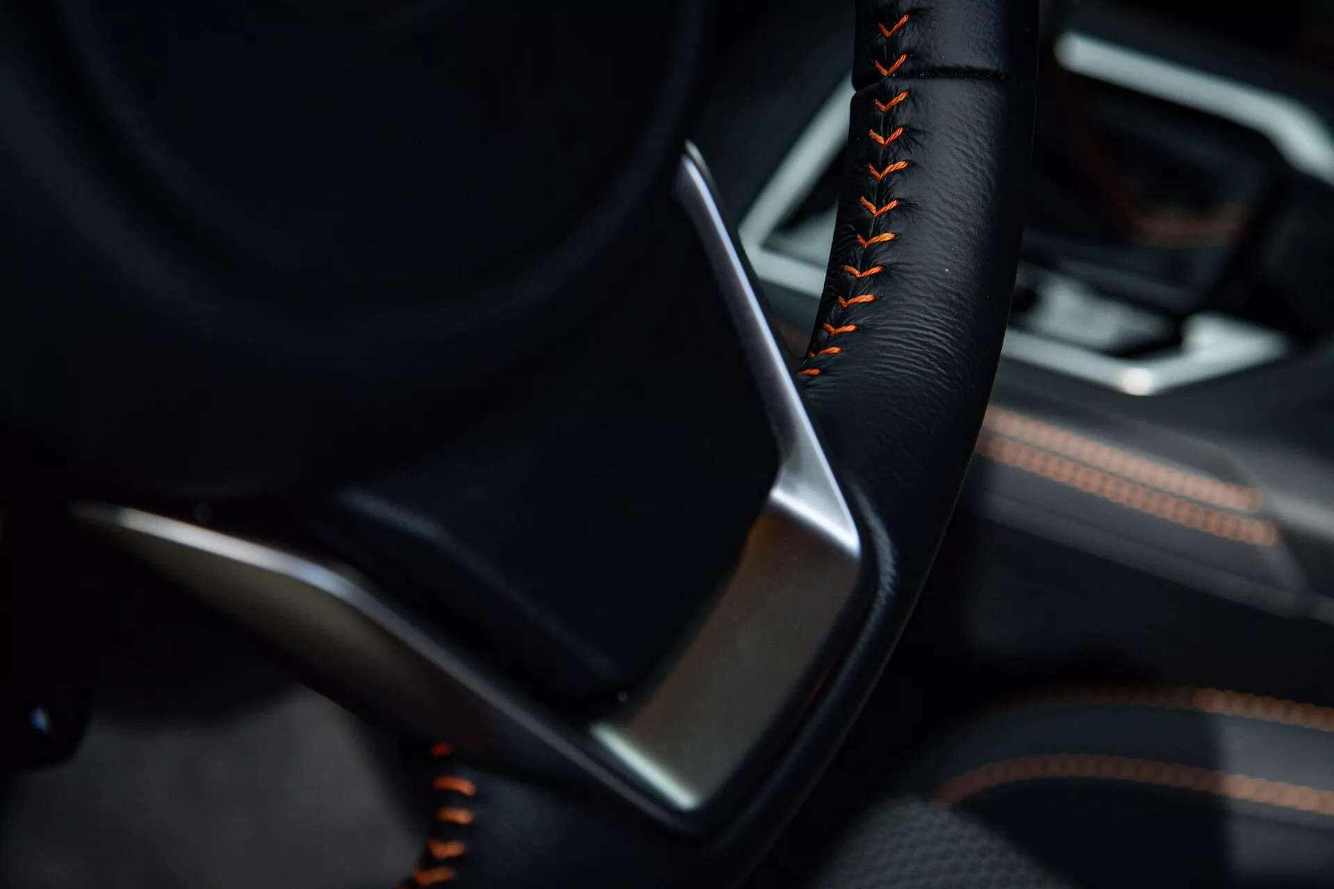 Detailný pohľad na interiér Subaru XV 2021 so zameraním na stranu vodiča s čiastočne viditeľným volantom vo farbe čiernej a oranžovým alebo červeným šitím, po boku dverného panelu s detailmi z čiernej kože alebo koženky a metalickými akcentmi