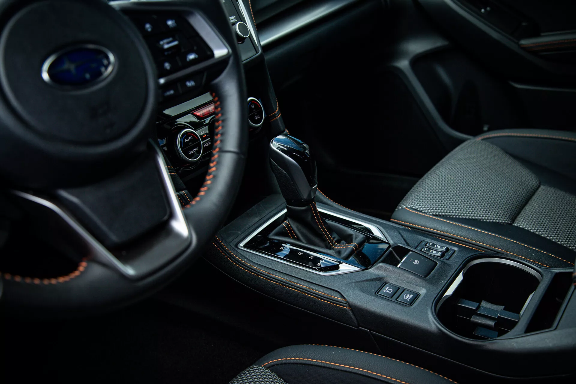 Detailný pohľad na interiér Subaru XV 2021 so zameraním na stredovú konzolu a oblasť radiacej páky z pohľadu spolujazdca, zobrazujúci multifunkčné tlačidlá na volante, automatickú radiacu páku s koženým čepom a kovovými akcentmi, a prvky luxusného interiéru, ako sú elektronická parkovacia brzda a systém klimatizácie.