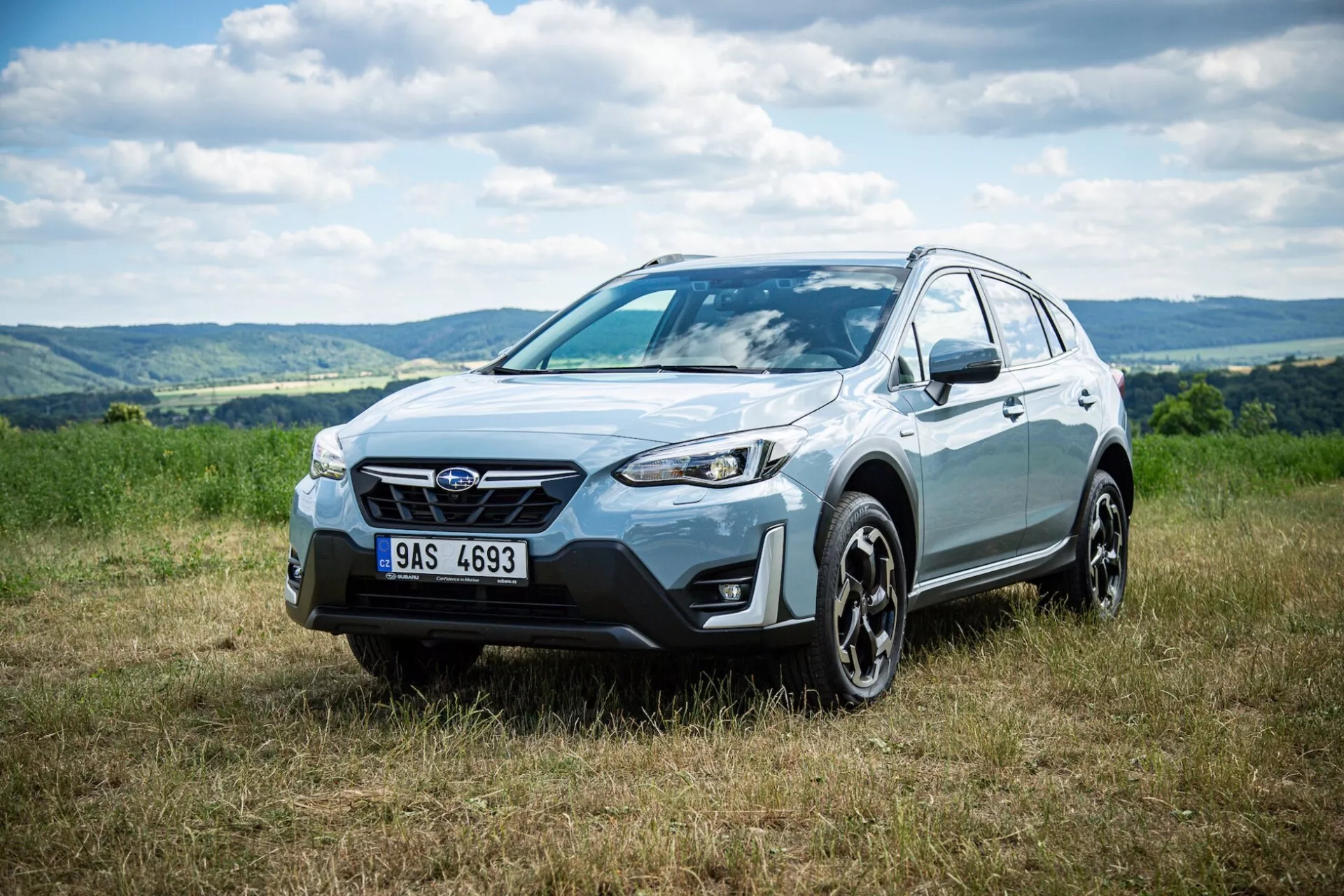 Crossover SUV Subaru XV 2021 zaparkované na tráve s kopcovitým pozadím, zdôrazňujúce prednú fasádu, bočný profil a dizajn kolesa