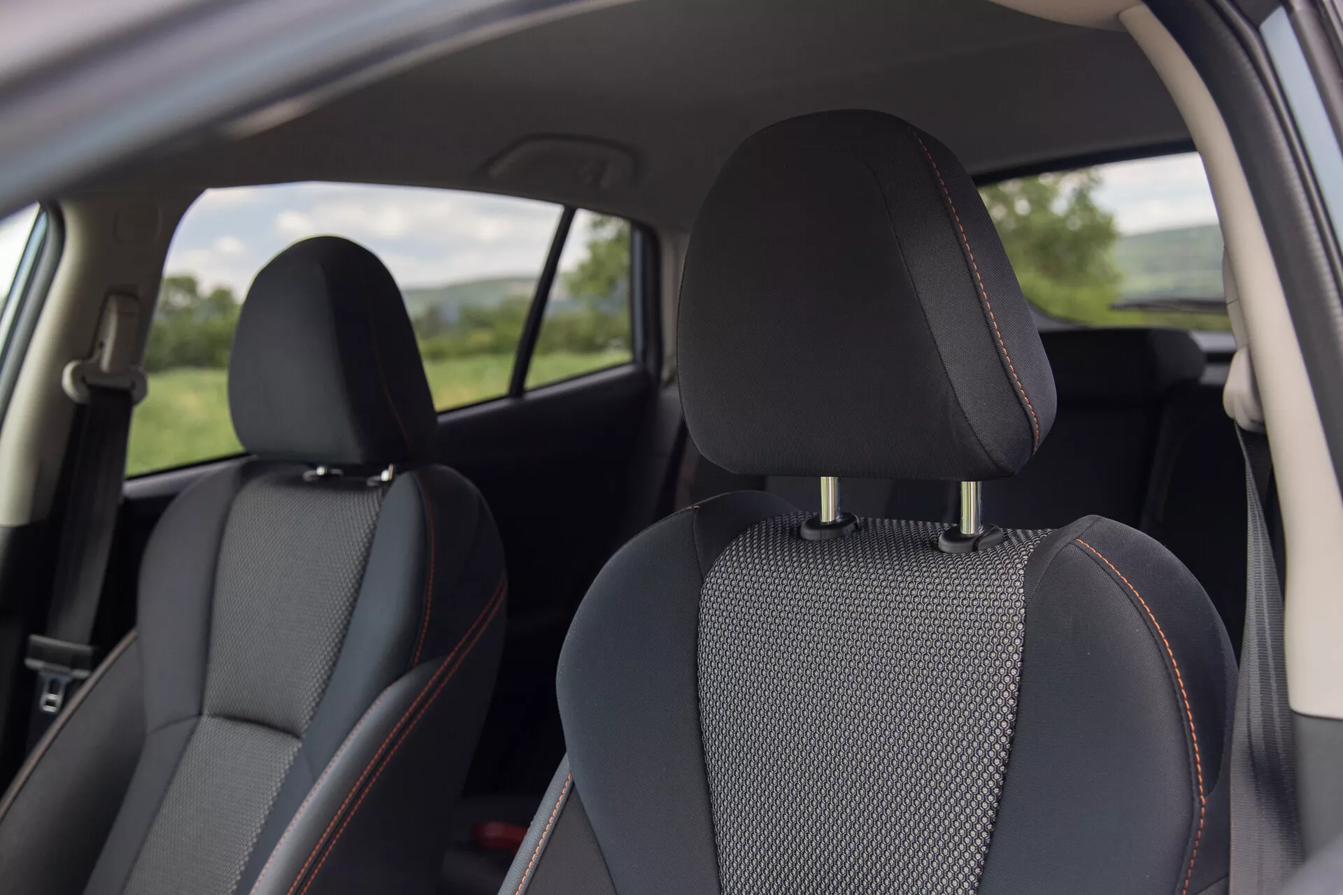 Interiérový pohľad na Subaru XV 2021 s čiernymi koženými sedadlami s vložkami zo vzorovaného materiálu a charakteristickými oranžovými stehmi, zameraný na pohodlie a dizajn z perspektívy zadného cestujúceho