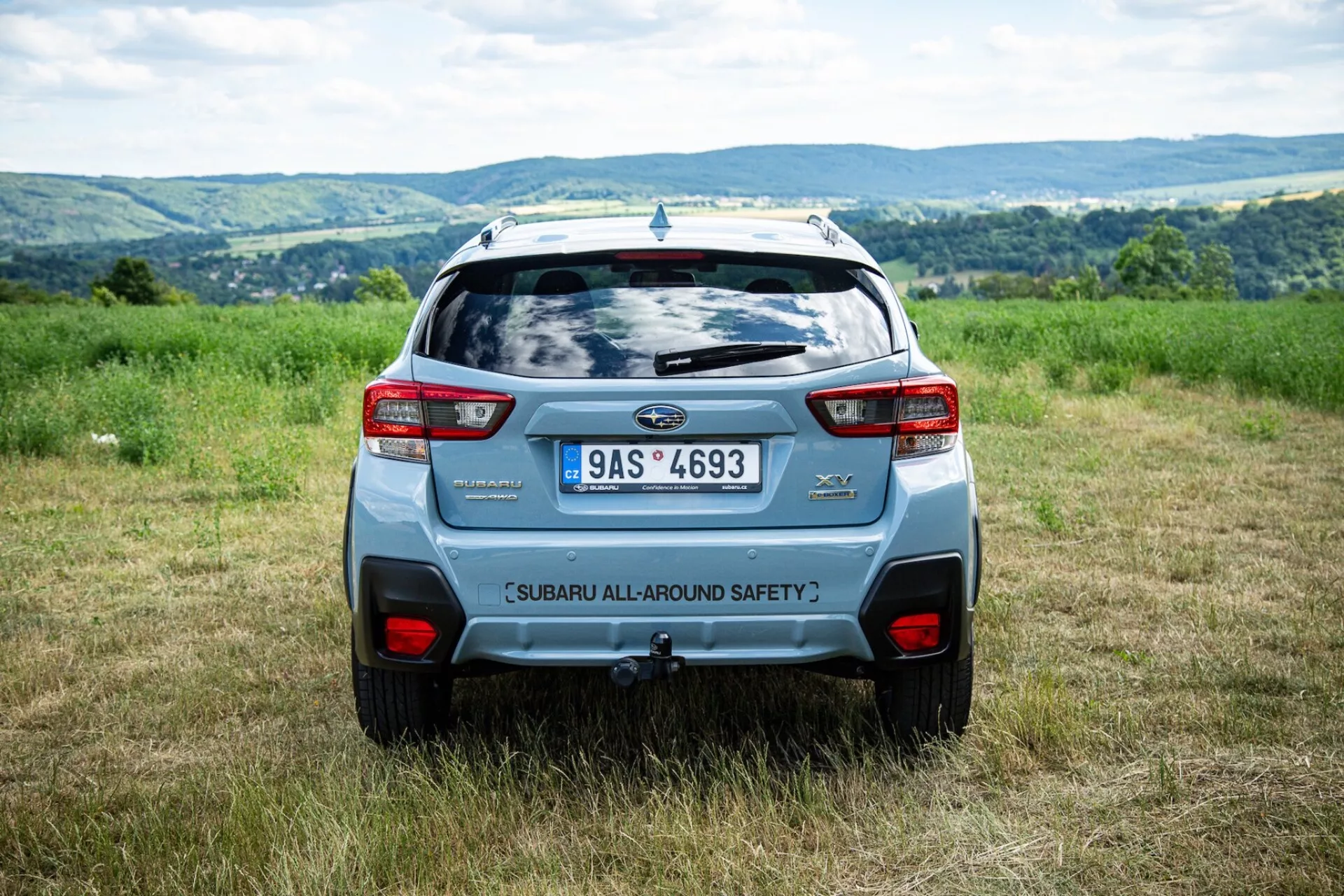 Zadný uhol pohľadu Subaru XV 2021 vonku na poli s kopcovitým pozadím, ktorý zdôrazňuje bezpečnostné prvky a moderné dizajnové prvky SUV ako zadný spojler a odvážne zadné svetlá