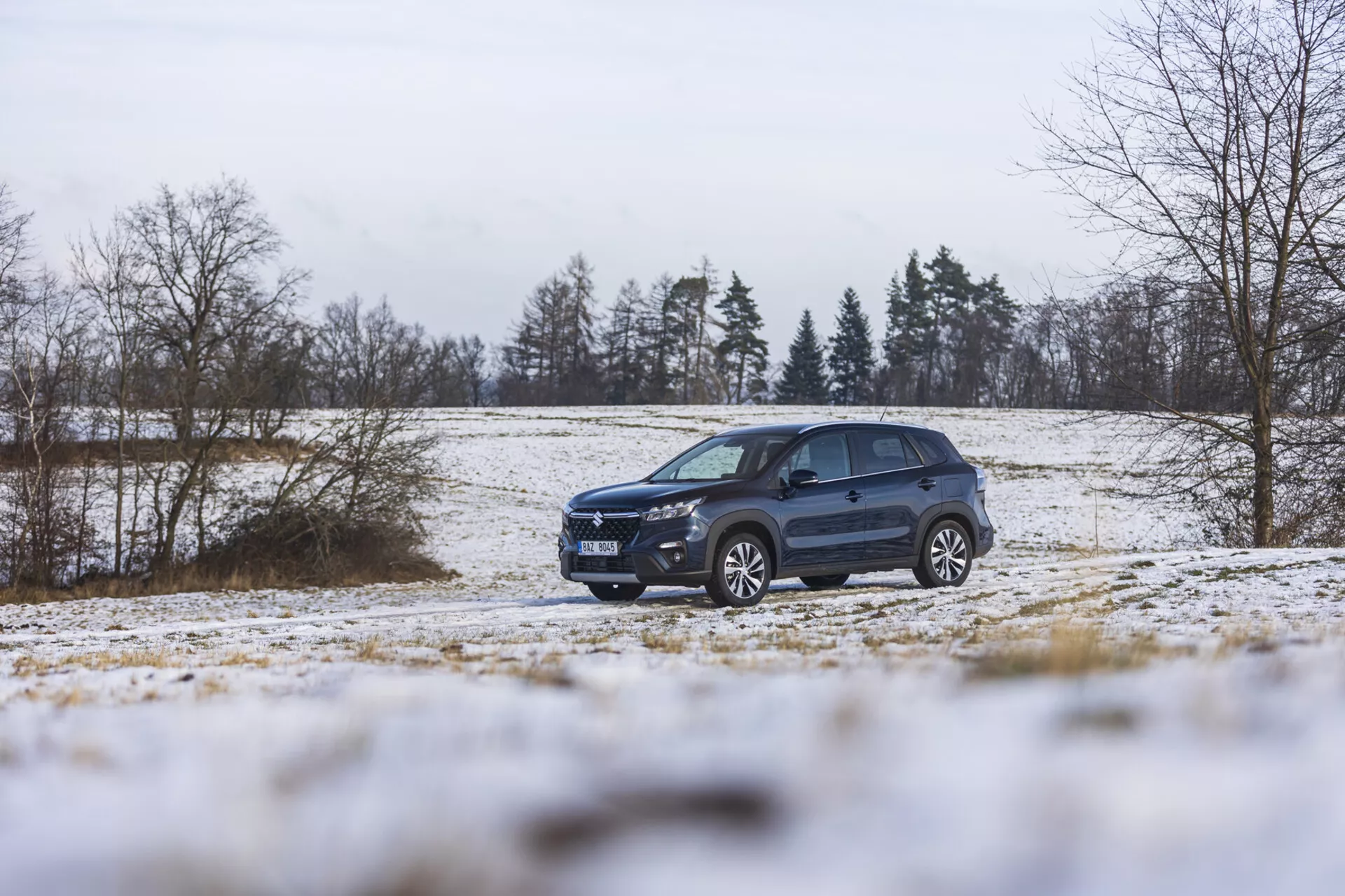 Suzuki S-Cross 2022 v zimnej krajine so snehom, ukazujúce jeho dynamický dizajn, pokročilé osvetlenie, zliatinové kolesá a strešné nosiče, zdôrazňujúce jeho štýl SUV a schopnosť jazdy v teréne.