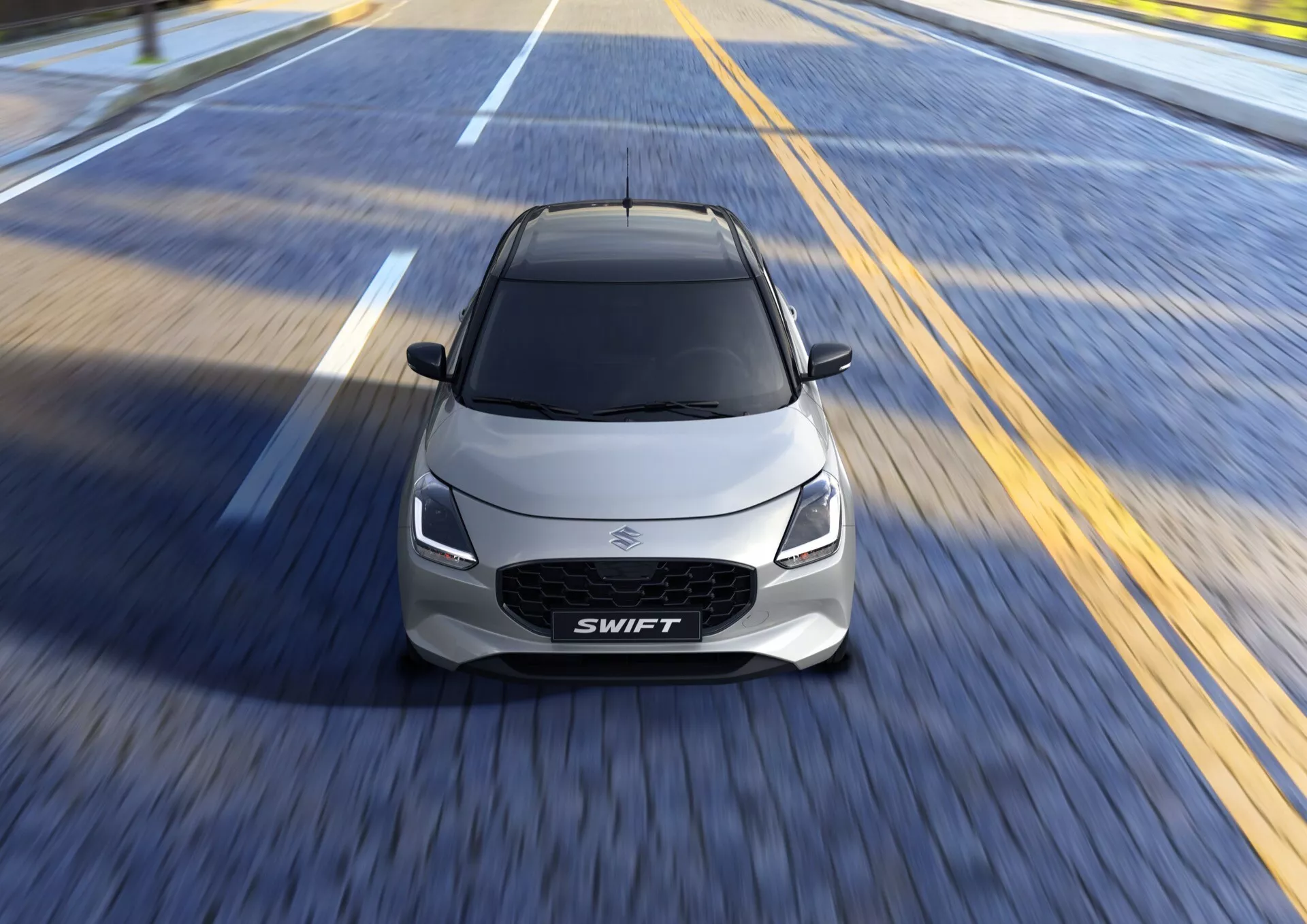 Suzuki Swift 7. generácie 2024 v pohybe na viacpásmovej ceste, predvádzajúci svoj aerodynamický dizajn, LED svetlomety a športové kontúry v prírodnom dennom svetle