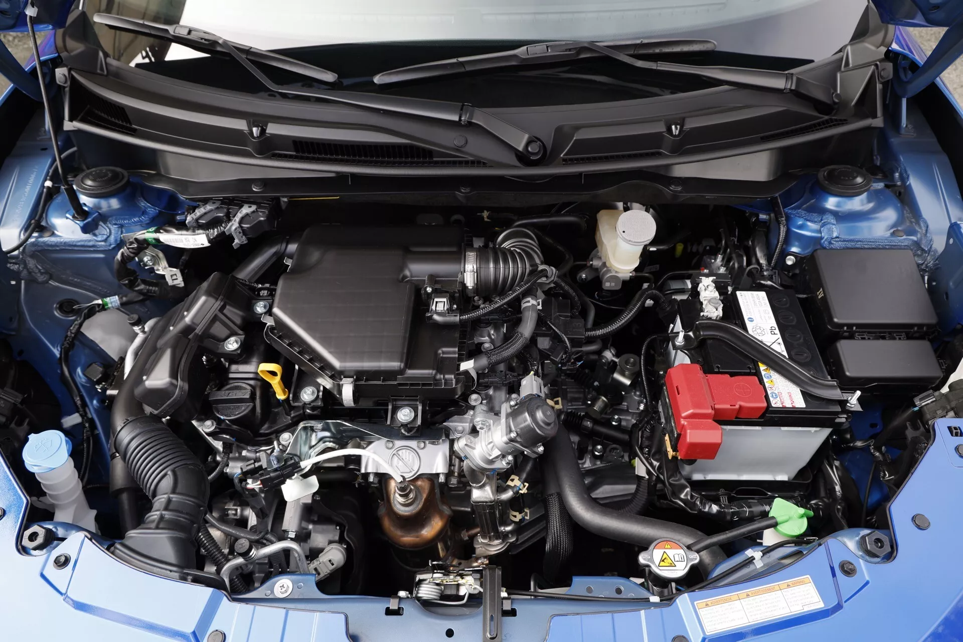 Podrobný pohľad zhora na motorový priestor Suzuki Swift 2024 zobrazujúci spaľovací motor, súbor nasávania vzduchu, nádrž na chladivo, autobatériu a rôzne údržbové komponenty