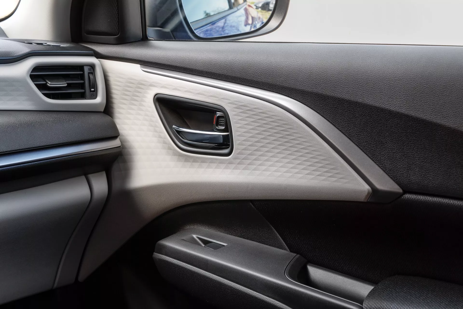Detail interiéru dverí vodiča Suzuki Swift 7. generácie 2024 s čalúnenou opierkou ruky, integrovaným elektronickým ovládacím panelom pre elektrické okná a ozdobnou lištou imitujúcou karbónové vlákna