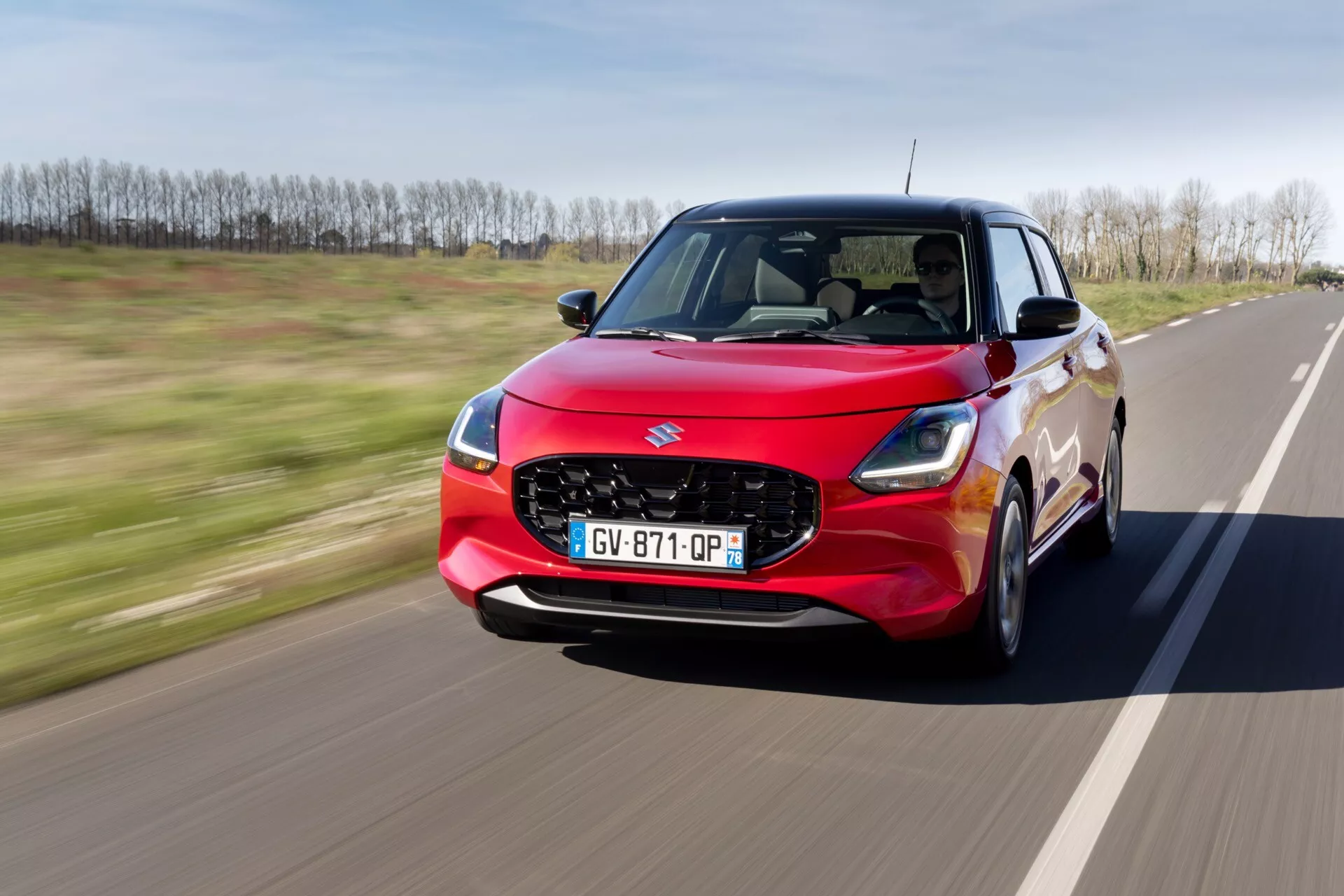 Suzuki Swift 7. generácie 2024 v pohybe, s výraznou červenou farbou, LED svetlometmi, aerodynamickou maskou a zliatinovými kolesami, ktoré prezentujú pokročilý dizajn a technológiu