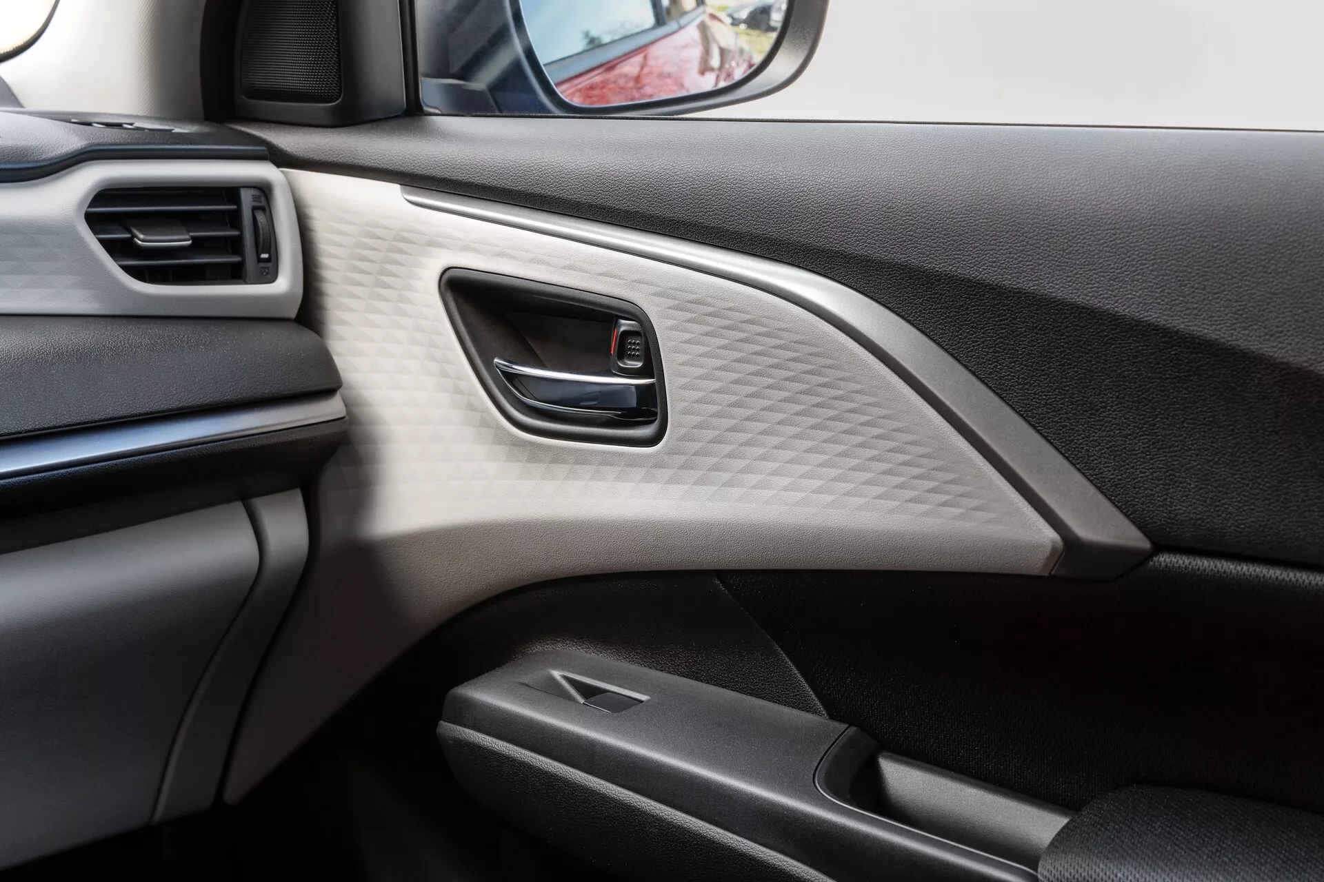 Interiér dverí auta Suzuki Swift 7. generácie 2024 s ergonomickou striebornou kľučkou, dekoratívnym panelom s uhlíkovým vzorom a materiálmi príjemnými na dotyk, z pohľadu vodiča alebo spolujazdca