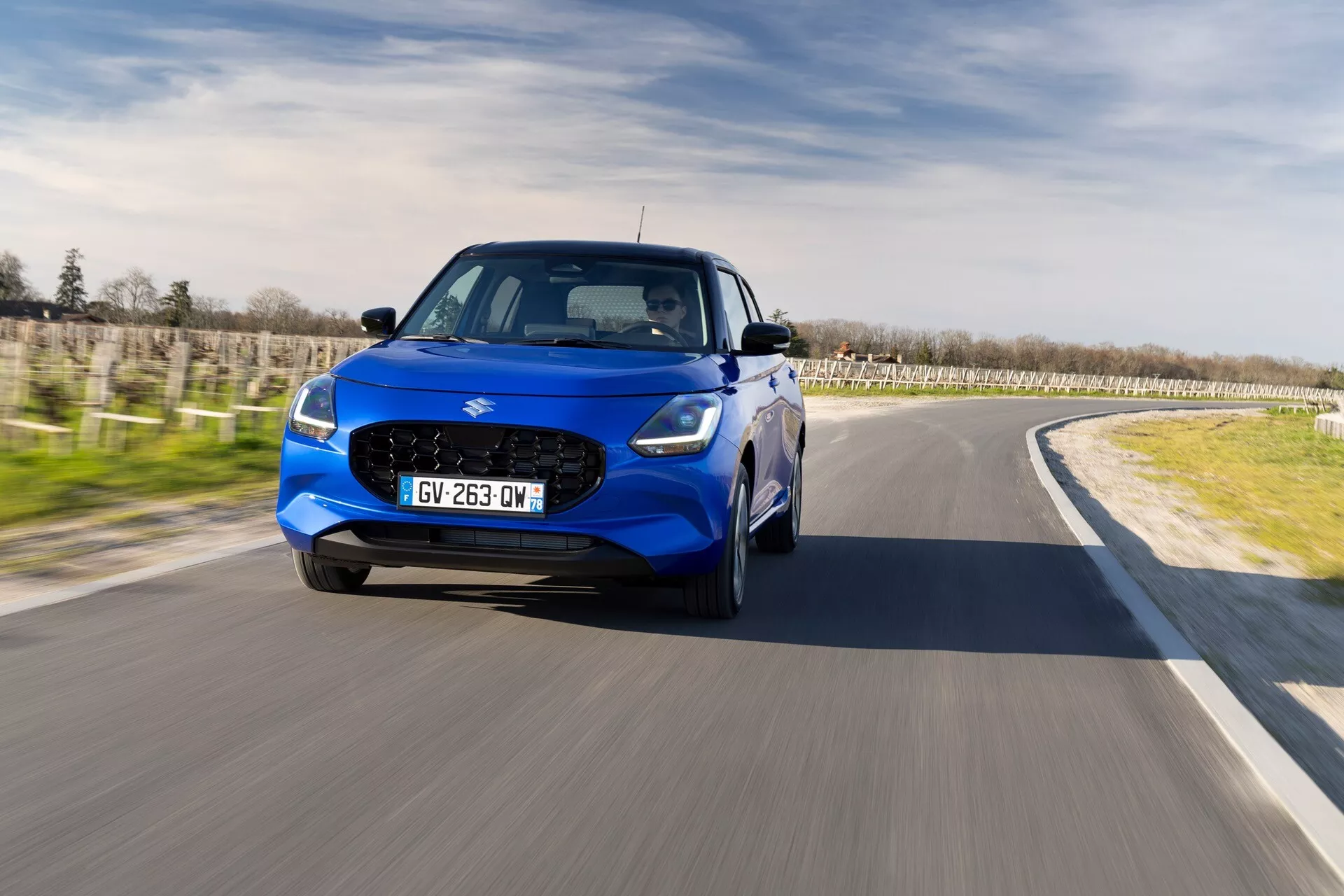 Suzuki Swift 2024 v pohybe, predvádzajúci svoj moderný dizajn a charakteristiky kompaktného crossoveru z uhla tri štvrtiny spredu s LED svetlometmi, mriežkovým predným grilom a športovými zliatinovými kolesami