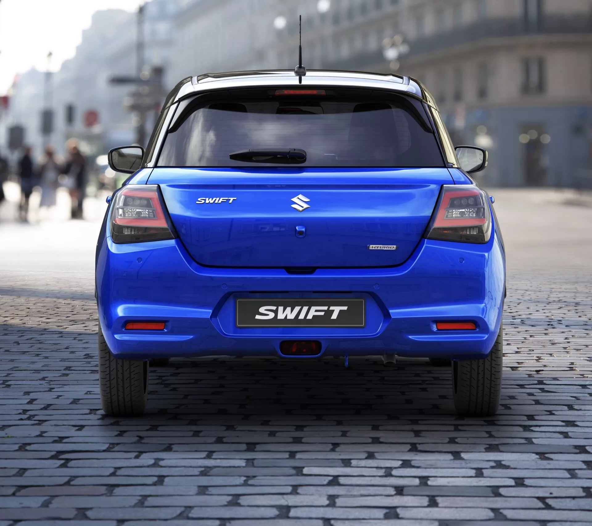 Zadný pohľad na Suzuki Swift 7. generácie 2024 zdôrazňujúci chrómový emblém, názov modelu SWIFT na veku batožinového priestoru, elegantný dizajn zadných svetiel a zadný stierač na dlažobnej ulici