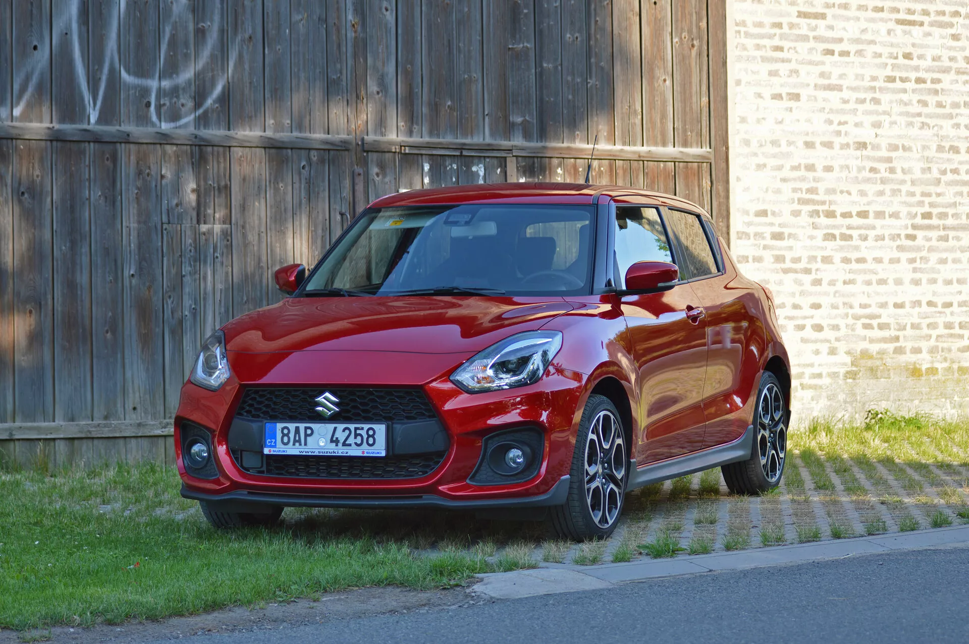 Suzuki Swift Sport 2017 v žiarivej červenej farbe, pohľad z troch štvrtín, predná strana, ukazujúci športový dizajn, ostré svetlomety, agresívnu prednú mriežku, hliníkové kolesá a aerodynamické bočné prahy