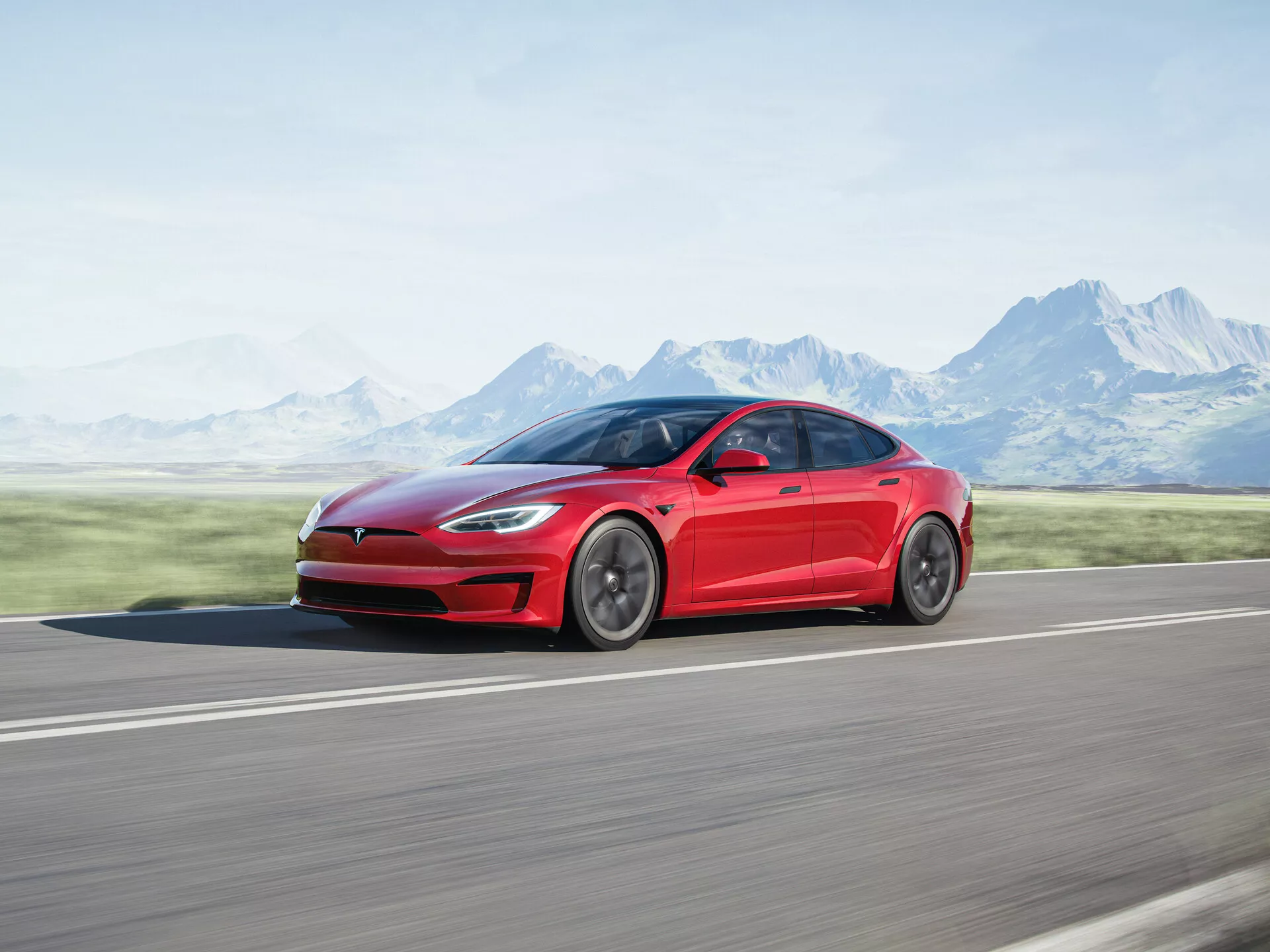 Bočný profilový záber elektrického sedanu Tesla Model S z roku 2016 (1. generácia facelift) v červenej farbe, zachytený v pohybe. Demonštruje sa elegantný a aerodynamický dizajn vozidla, s hladkými líniami od predného blatníka po zadnú časť a leštenými ráfikmi. Fotografované na asfaltovej ceste s rozmazaným pozadím hôr a jasnej oblohy, zdôrazňujúc rýchlosť a pohyb vozidla.