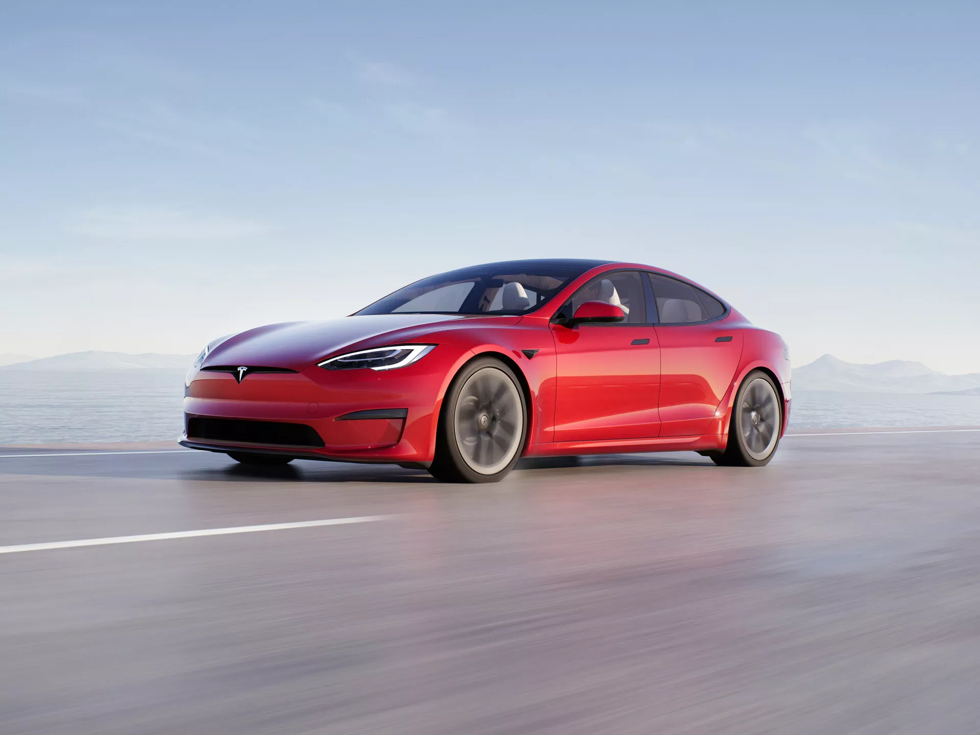 Obrázok zobrazuje moderný štvordverový sedan Tesla Model S 2016 (1. generácia facelift) v pohybe na hladkej ceste alebo trati. Vozidlo je prezentované z nízkeho uhla bočného profilu, takže sú jasne viditeľné jeho elegantné a aerodynamické línie, vrátane charakteristickej uzavretej mriežky, úzkych LED svetlometov a hladkého predného nárazníka. Dizajn fastback s jemne sa zvažujúcou strechou, zapustenými vysúvacími kľučkami dverí a minimálnymi aerodynamickými zrkadlami zdôrazňuje zameranie vozidla na aerodynamiku. Veľké kolesá s mnohými lúčmi naznačujú optimalizáciu prúdenia vzduchu a zníženie odporu. Kompozícia používa rozostrenie pohybu na vyjadrenie vysokej rýchlosti, pričom samotné auto je ostro zaostrené na rozostrenom pozadí. Tento profesionálny fotografický záber zdôrazňuje elektrickú povahu vozidla, pokročilé osvetlenie, aerodynamický dizajn a potenciálne asistenčné funkcie vodiča.