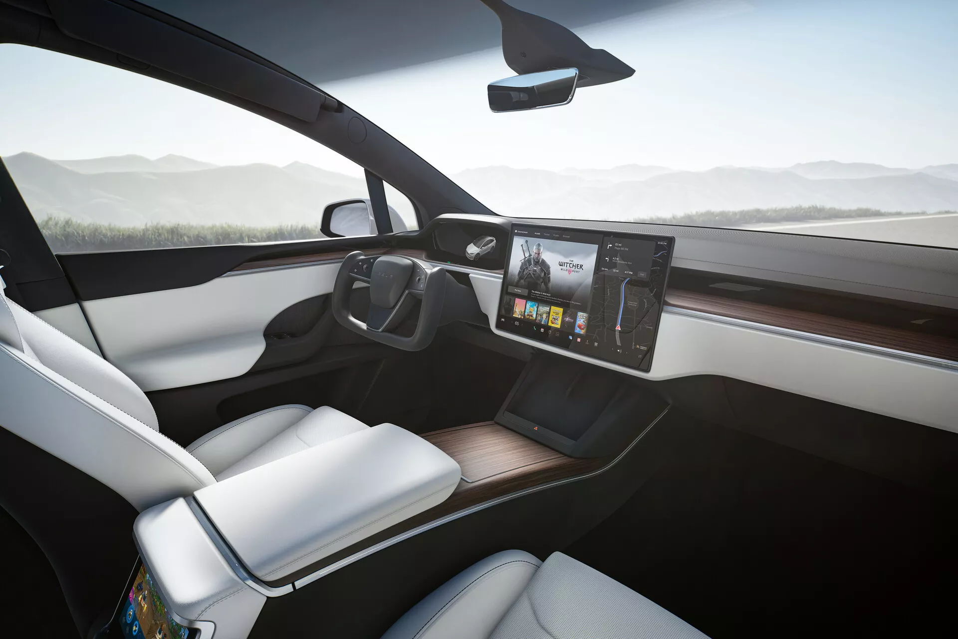 Interiér Tesla Model X 2021, zobrazený z mierne nakloneného uhla na stranu spolujazdca, s modernou prístrojovou doskou a veľkým, centrálne umiestneným dotykovým infotainment systémom s farebnými grafikami. Biely poťah sedadla spolujazdca kontrastuje elegantne s tmavšou palubnou doskou a dreveným obložením. Smartphone leží na potenciálnej bezdrôtovej nabíjacej podložke na čistom stredovom konzole a veľké predné okná prispievajú k vzdušnosti a otvorenému pocitu kabíny. Štíhle spätné zrkadlo na hornom strede čelného skla naznačuje pokročilé funkcie, ako sú automatické stmavovanie alebo zobrazenie zadnej kamery.