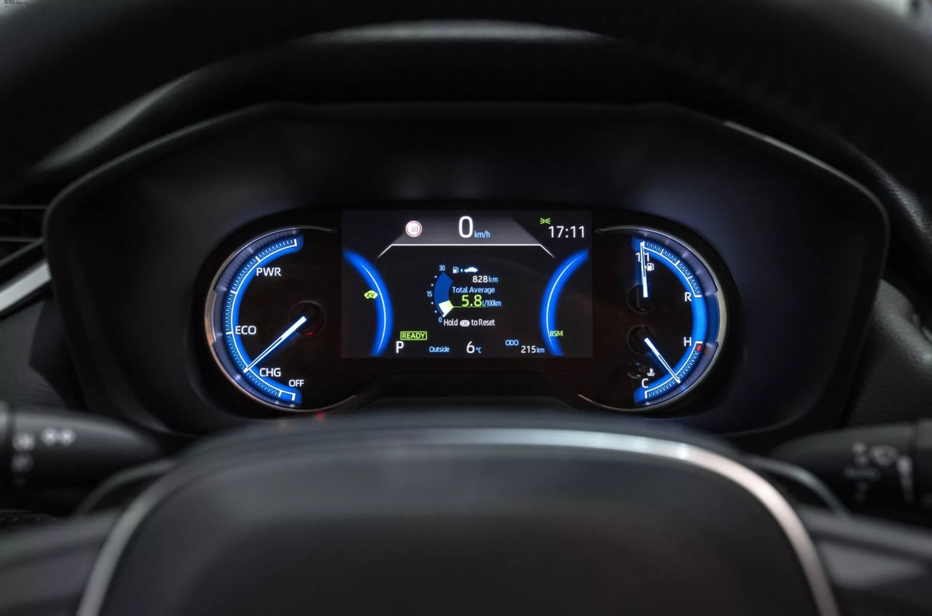 Detailný pohľad na prístrojový panel Toyota RAV4 2019 ukazujúci hybridné meracie prístroje s meračom výkonu, rýchlosťomerom a centrálnym digitálnym displejom zobrazujúcim statickú pozíciu, palivovú efektivitu a vonkajšiu teplotu z pohľadu vodiča.